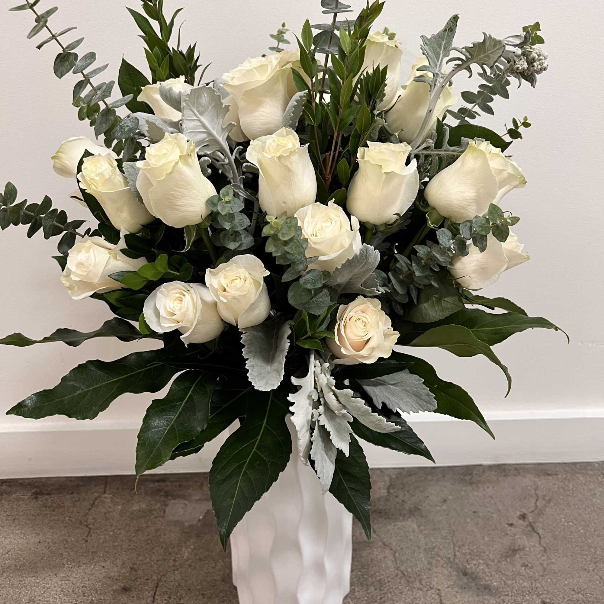 White roses arranged in a tall white vase with silver-green foliage, photo 3 of 4