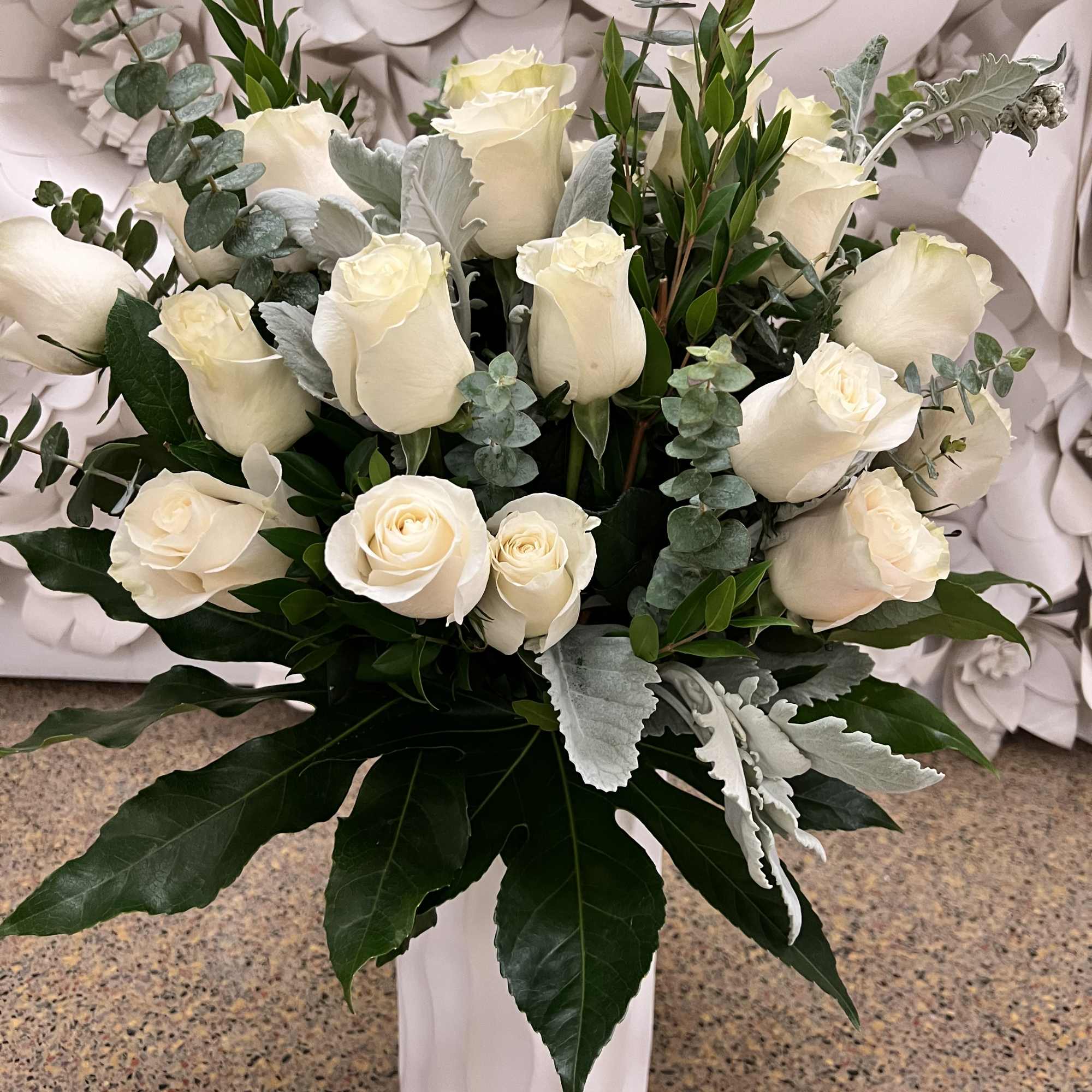 White roses arranged in a tall white vase with silver-green foliage, photo 4 of 4