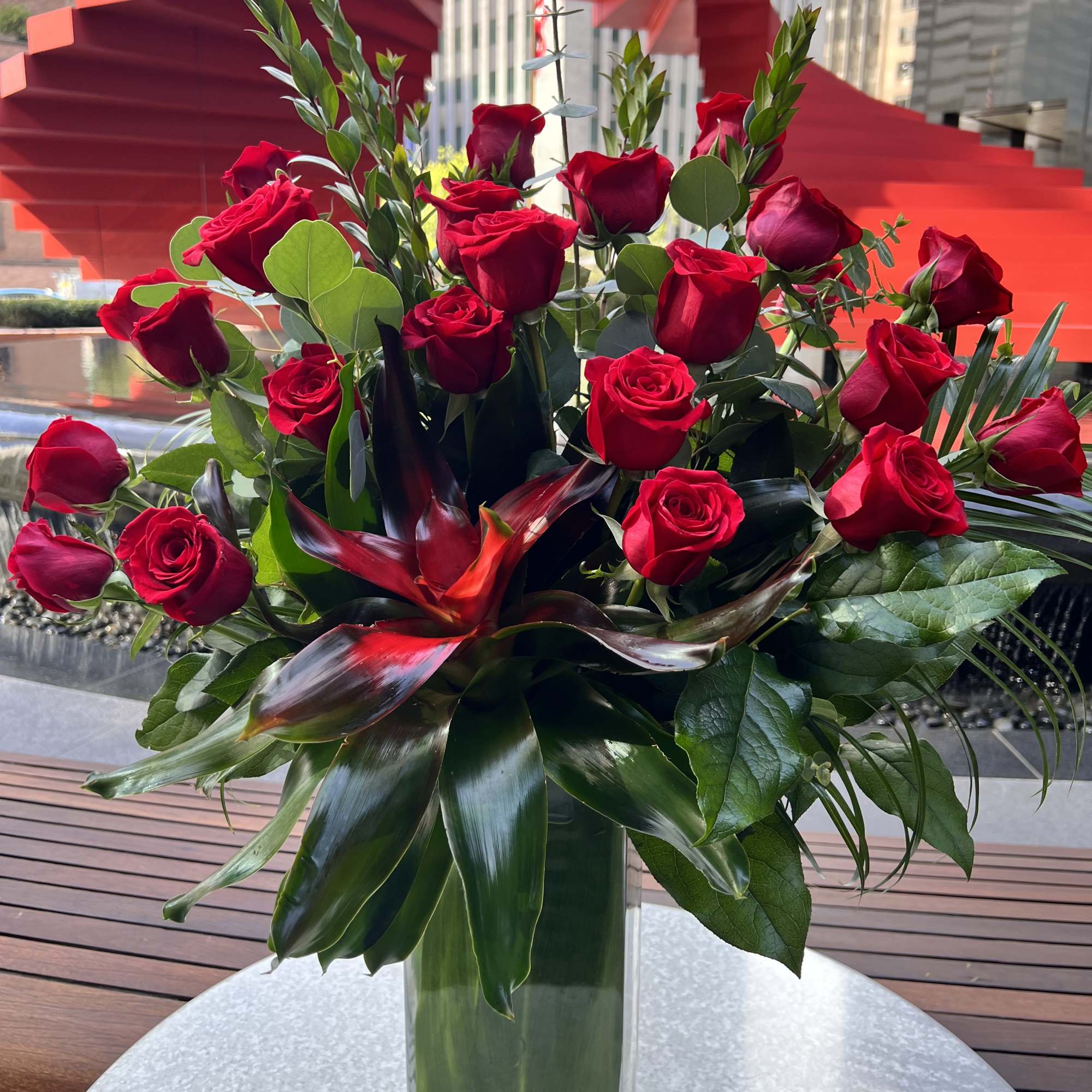 Red roses arranged in a tall clear glass vase with tropical foliage