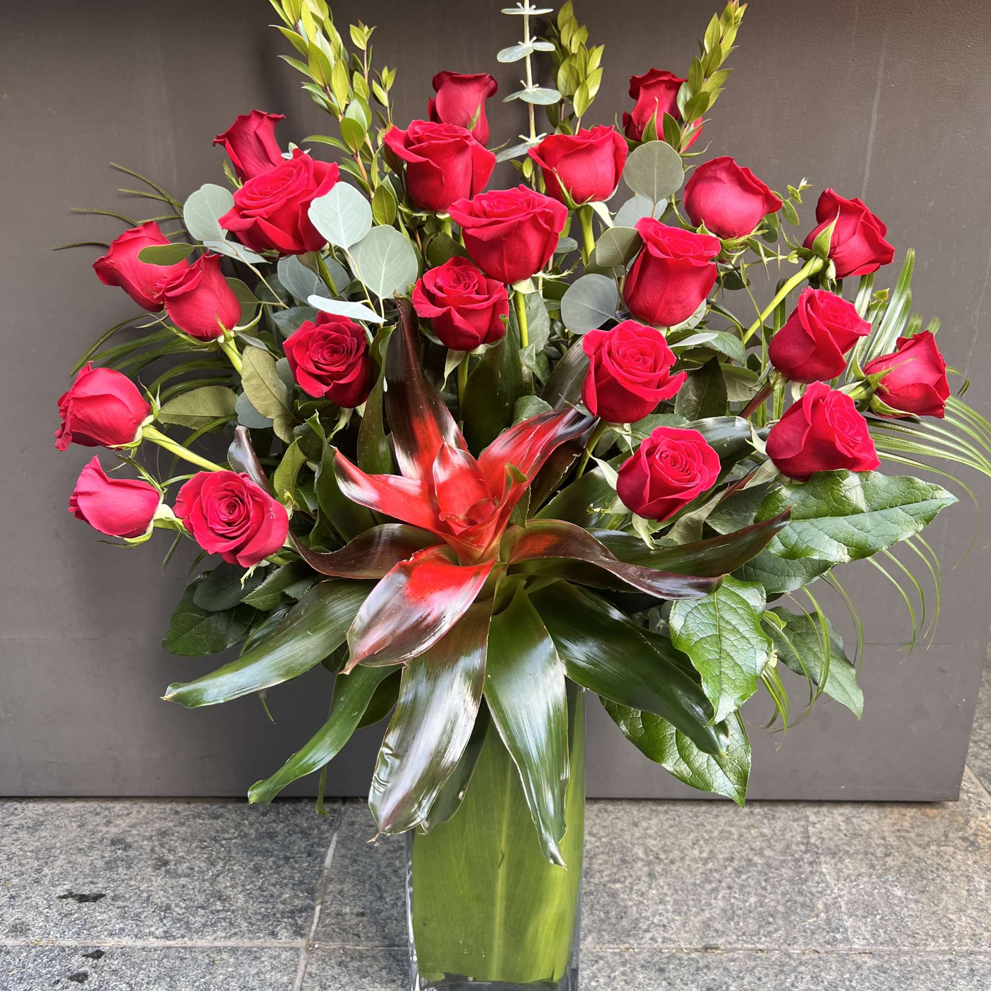 Red roses arranged in a tall glass vase with tropical foliage, photo 4 of 4