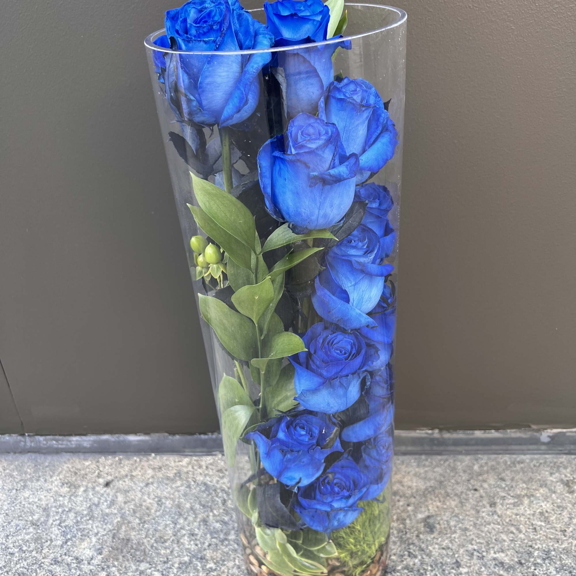 Blue roses arranged in a tall clear glass vase