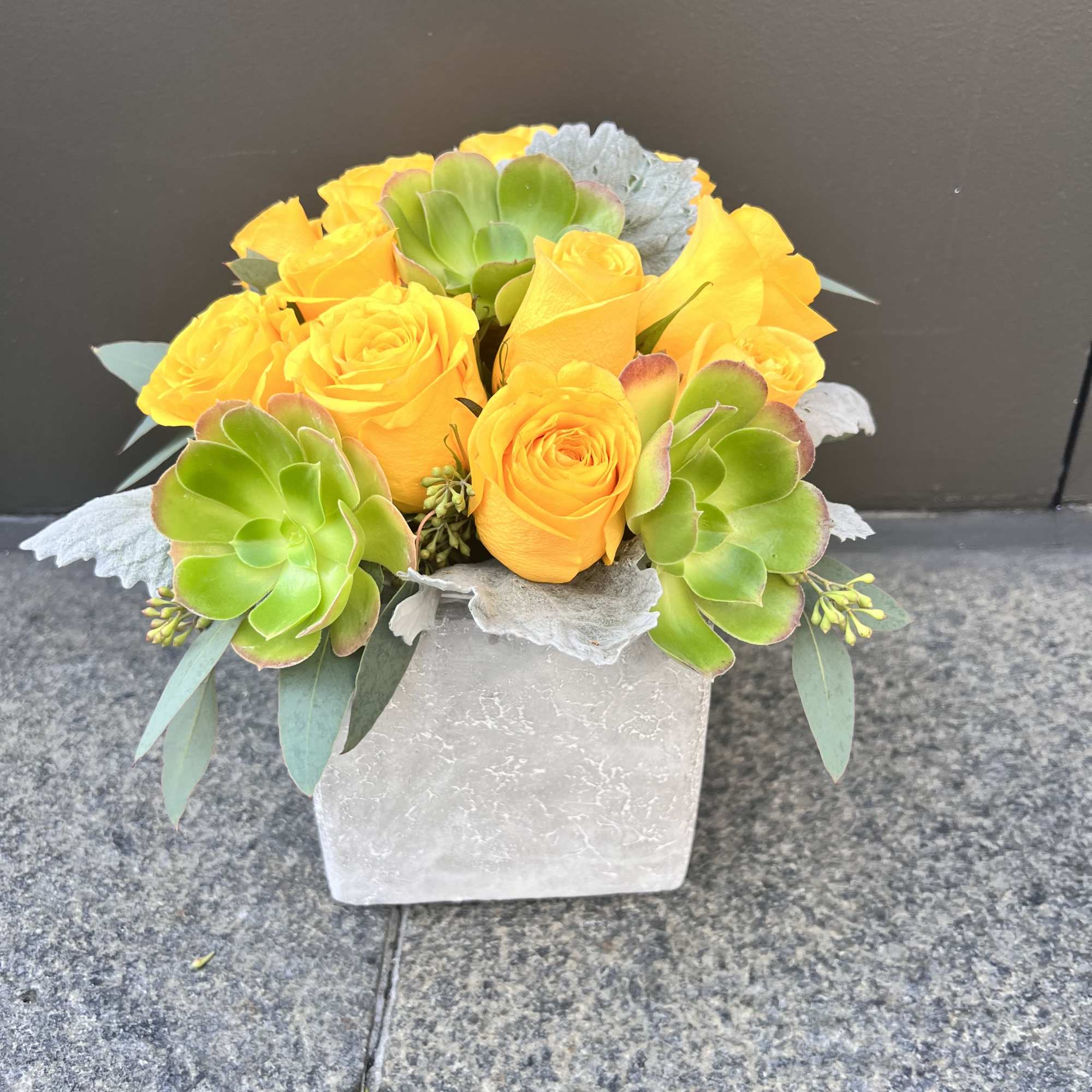 Yellow roses and green succulents in a square vase