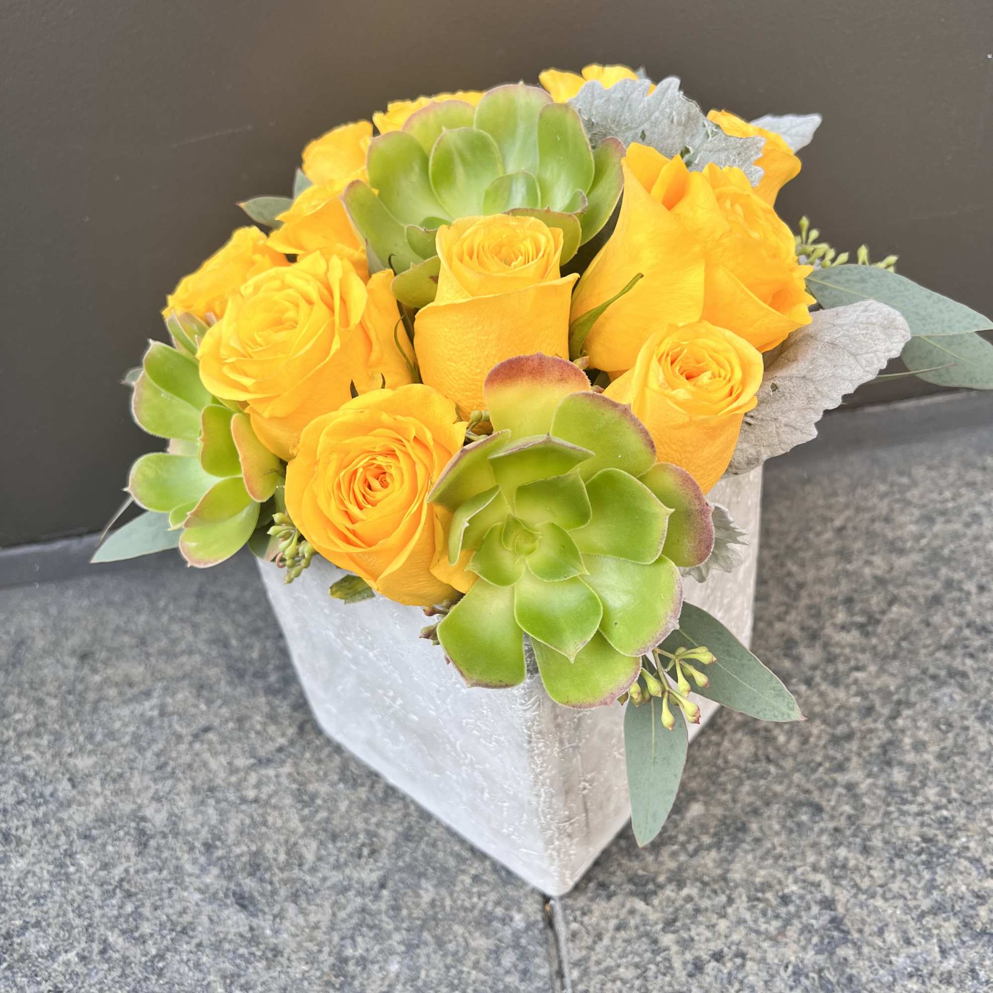 Yellow roses and green succulents in a white vase