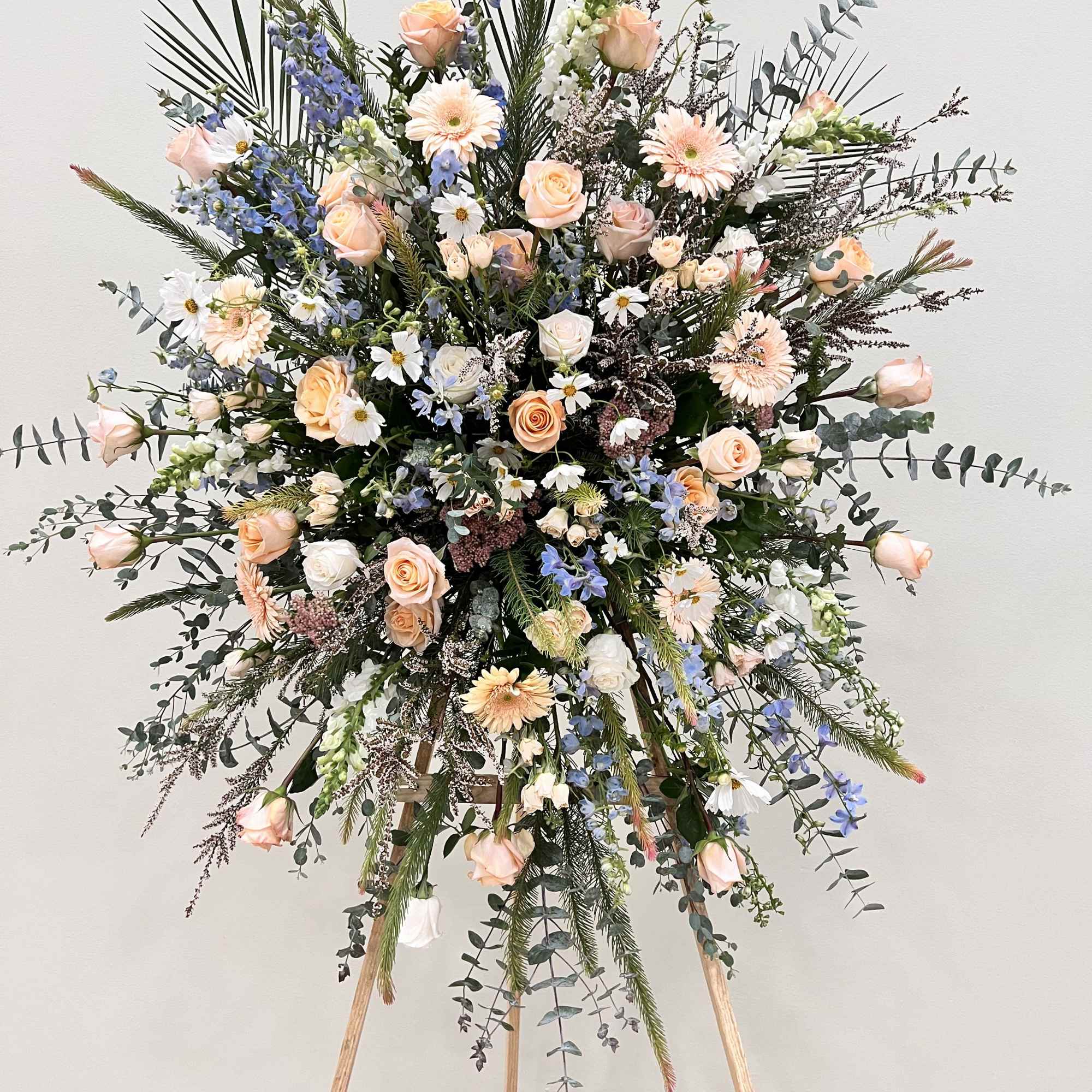 Large standing floral spray with peach roses and blue flowers on an easel