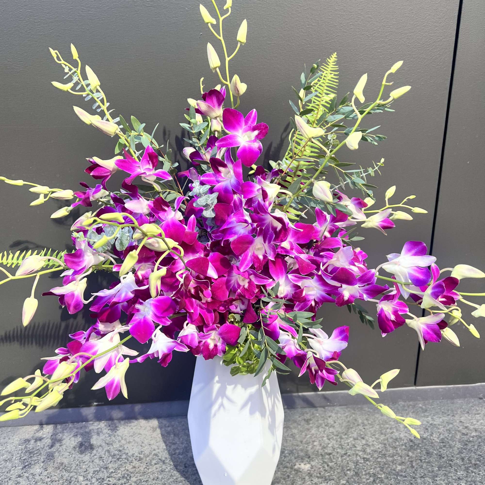 Tall bouquet of purple orchids in a white vase