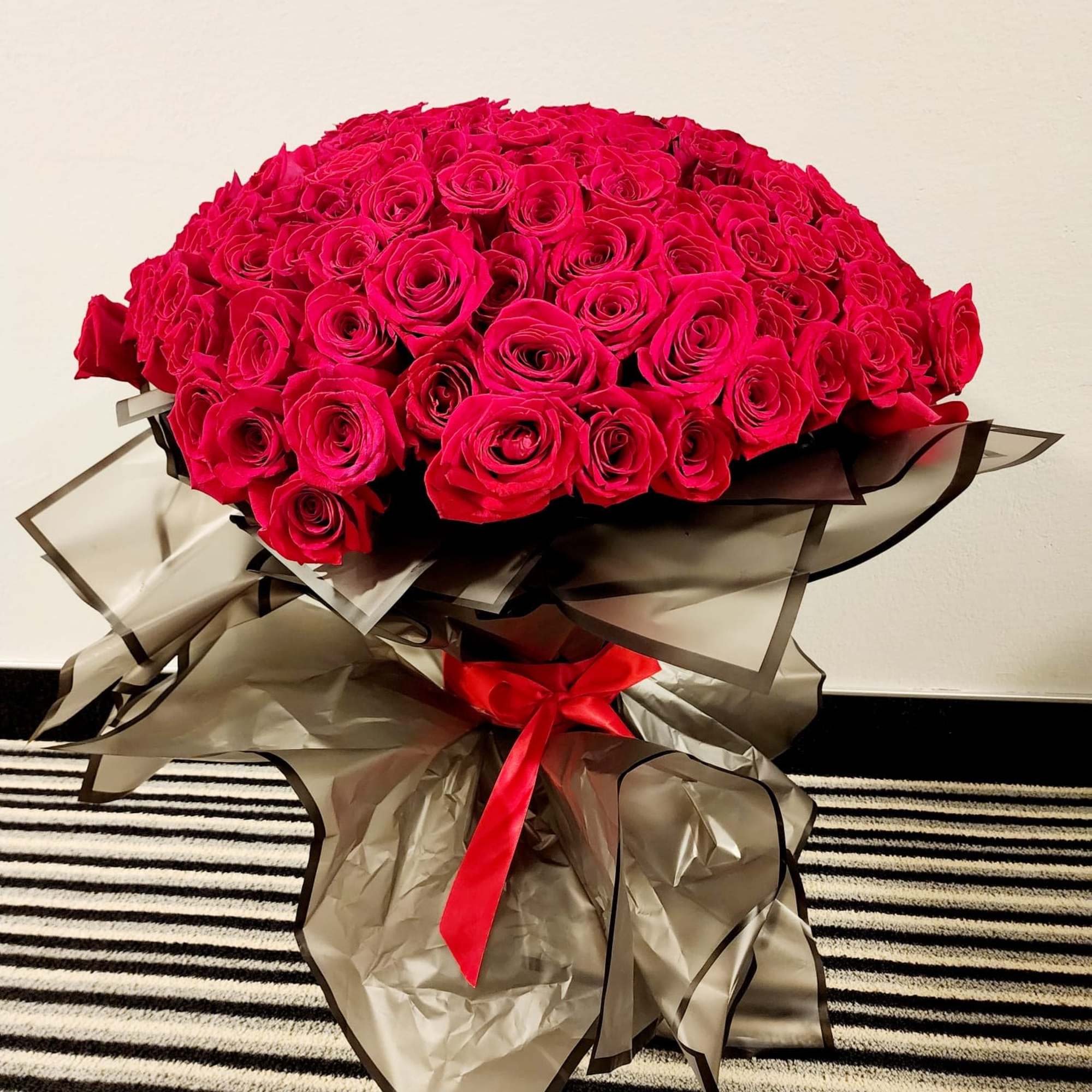 Large bouquet of hot pink roses wrapped in dark translucent paper with a red ribbon
