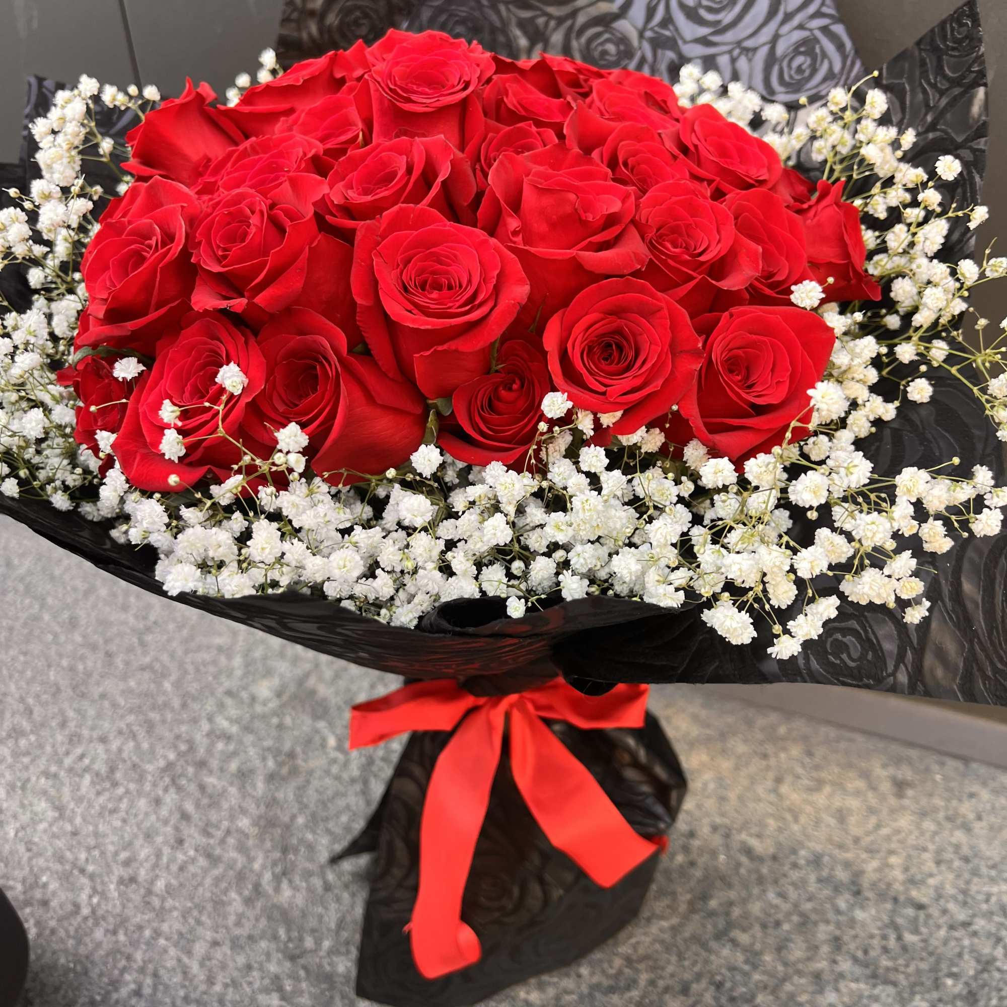 Bouquet of red roses with white baby's breath in black wrap and red ribbon