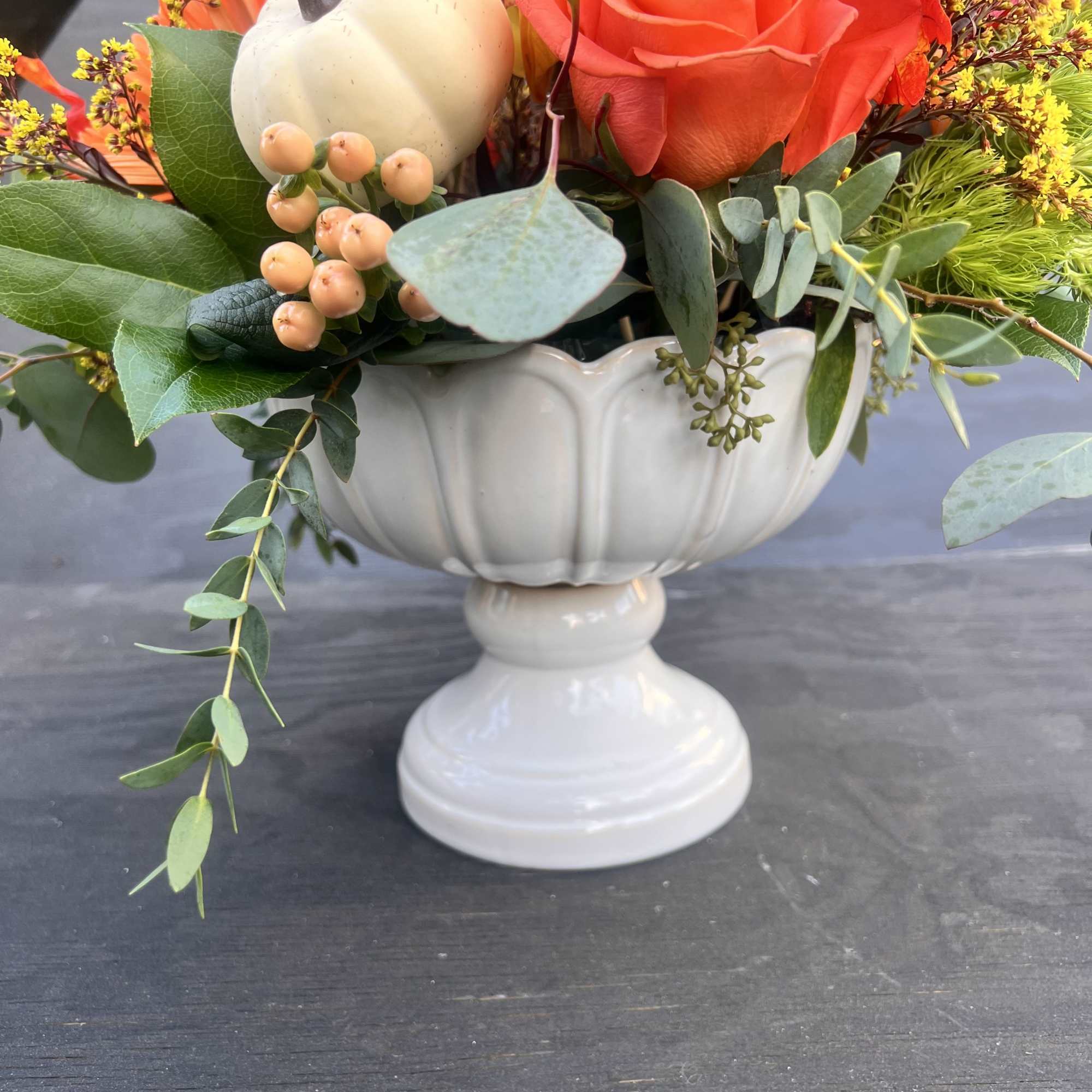 Orange roses in a white pedestal vase with a small pumpkin accent