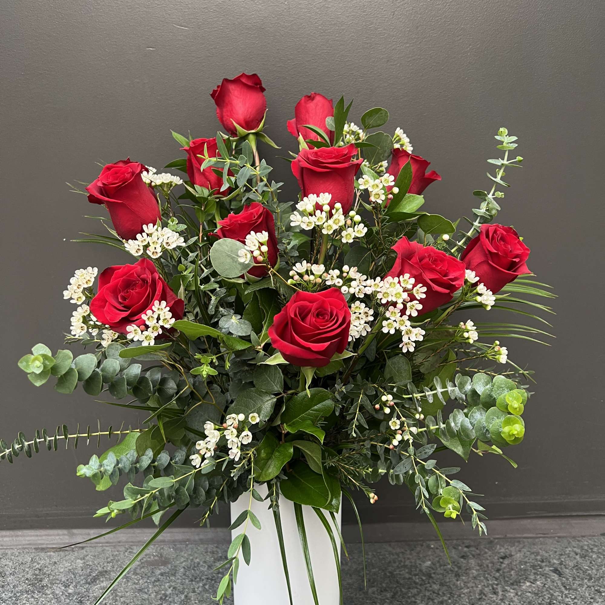 Red roses arranged in a tall white vase with white filler flowers
