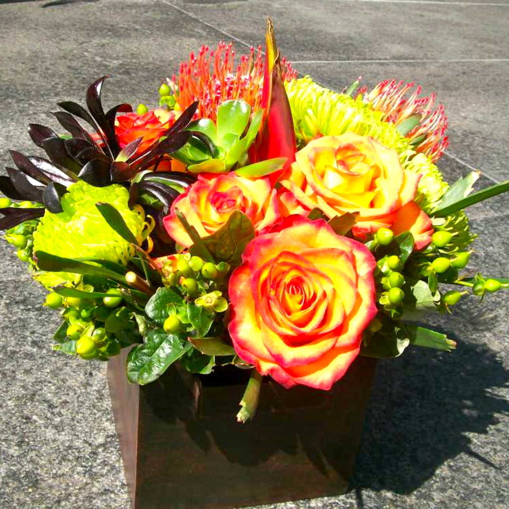 Bright mixed bouquet with orange-yellow roses in a square vase