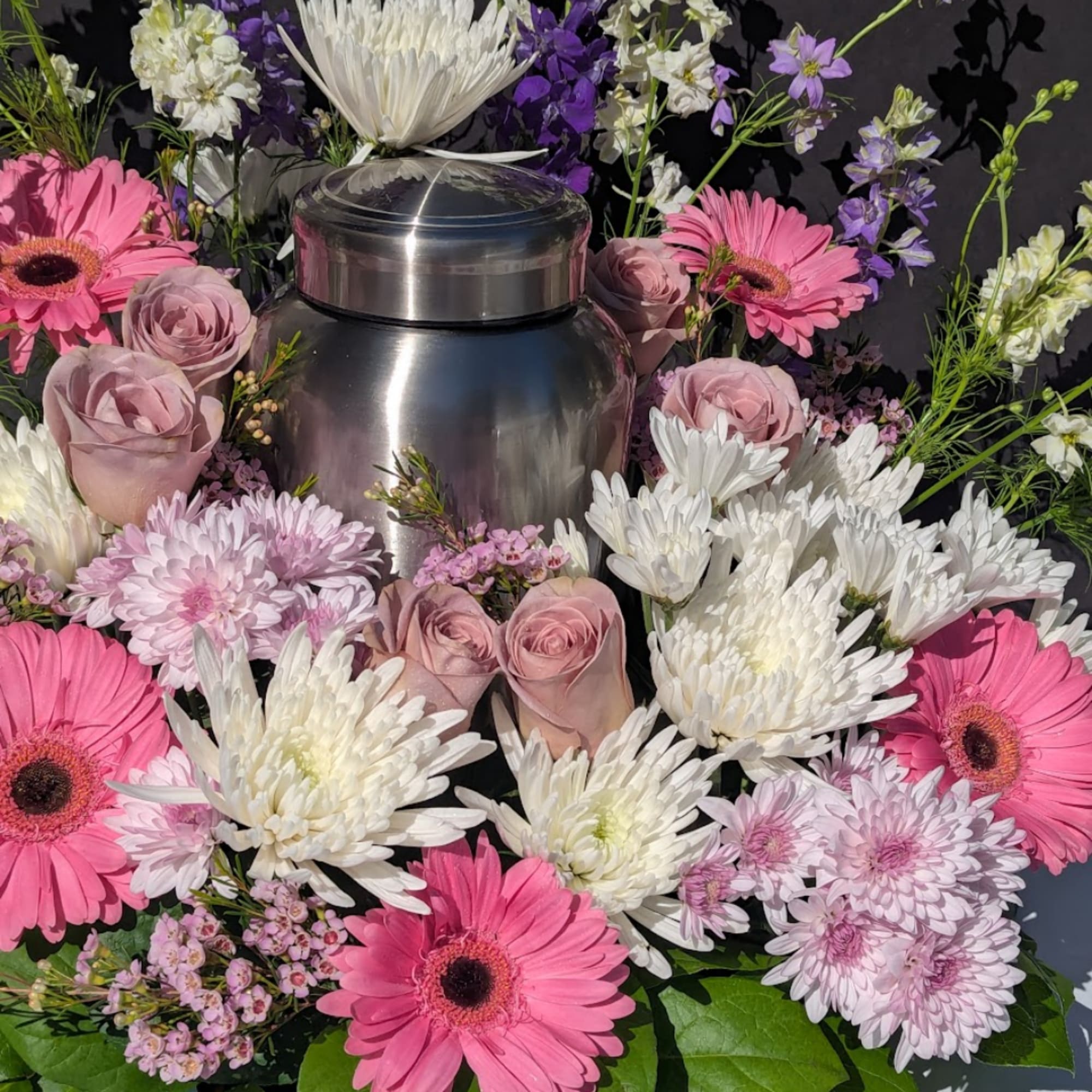 Pink and white flowers arranged around a stainless steel urn.