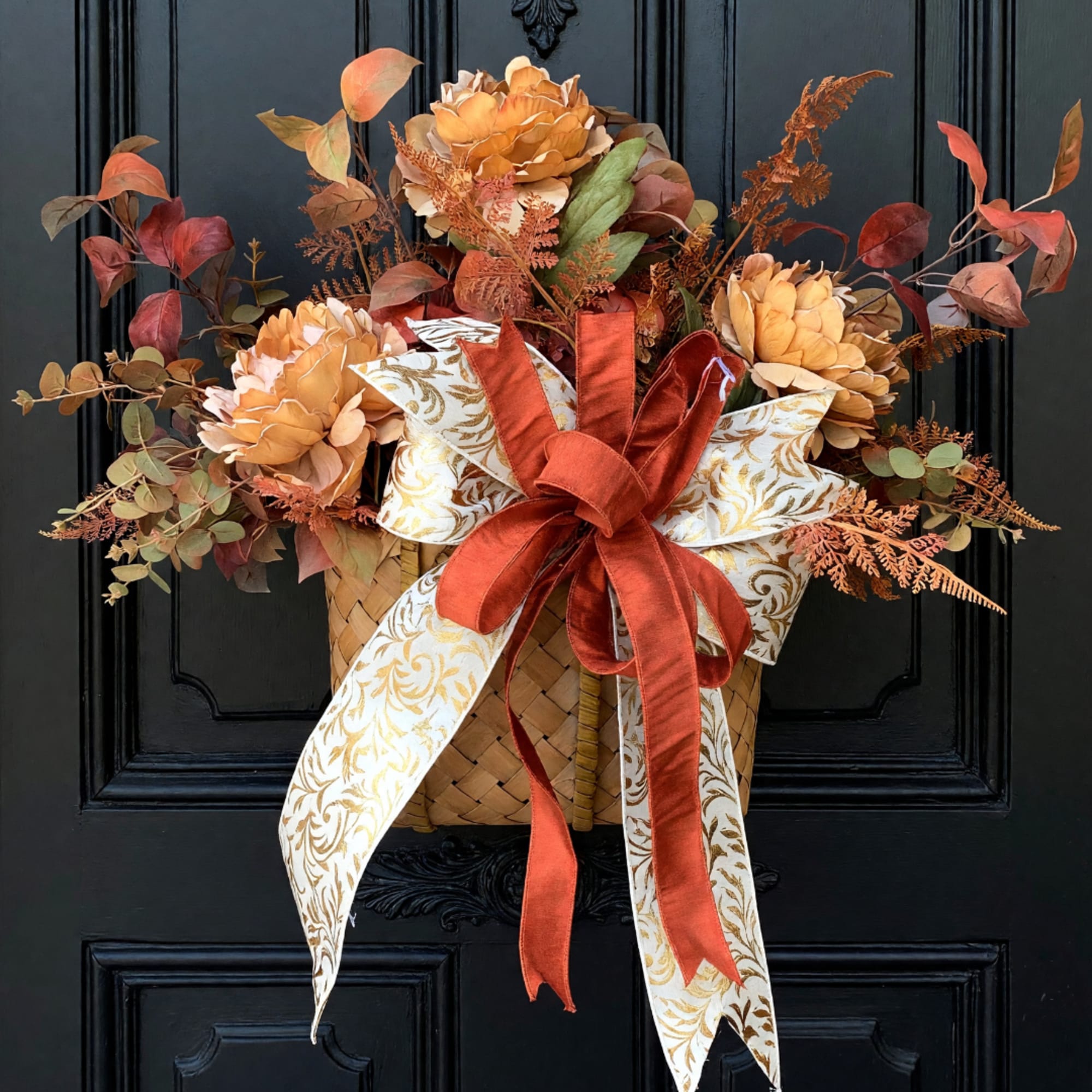 Autumn floral basket with orange blooms, ribbon, and patterned bow on a black door