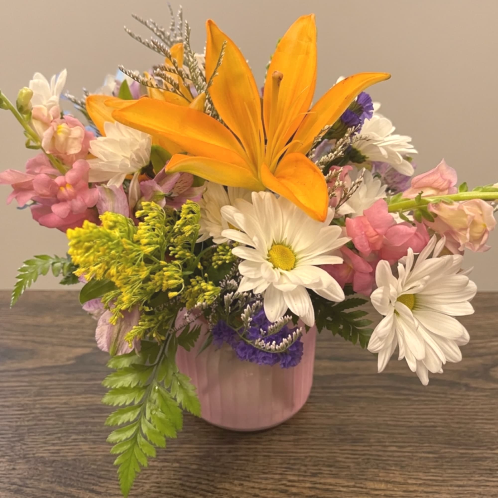Mixed bouquet with orange lily, white daisies, and pink flowers in a pink vase