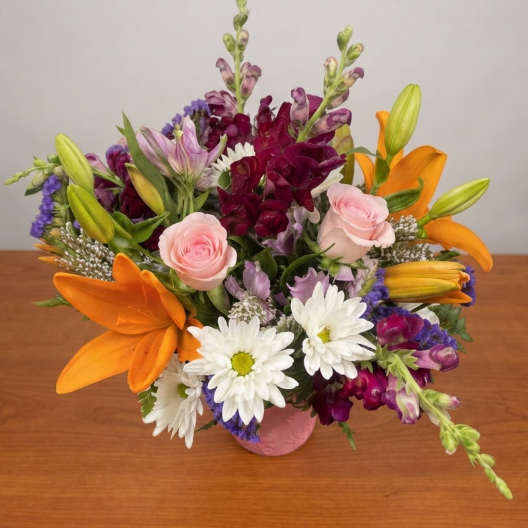 Mixed bouquet with orange lilies, pink roses, and white daisies in a pink vase