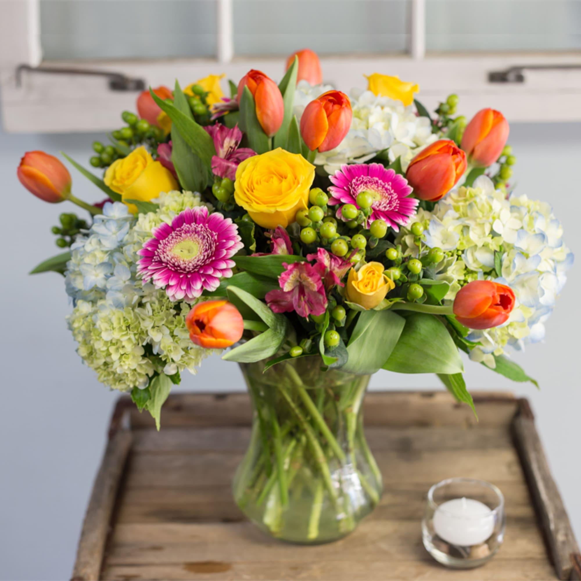 Mixed bouquet of tulips, roses, gerbera daisies, and hydrangeas in a glass vase
