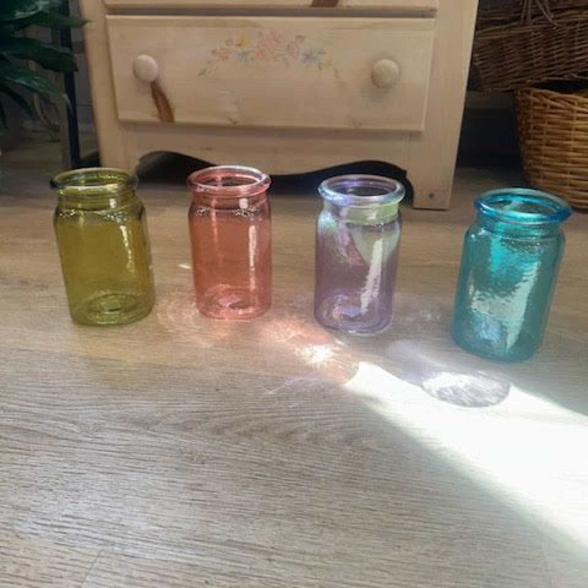 Four small colored glass jars on a wooden floor