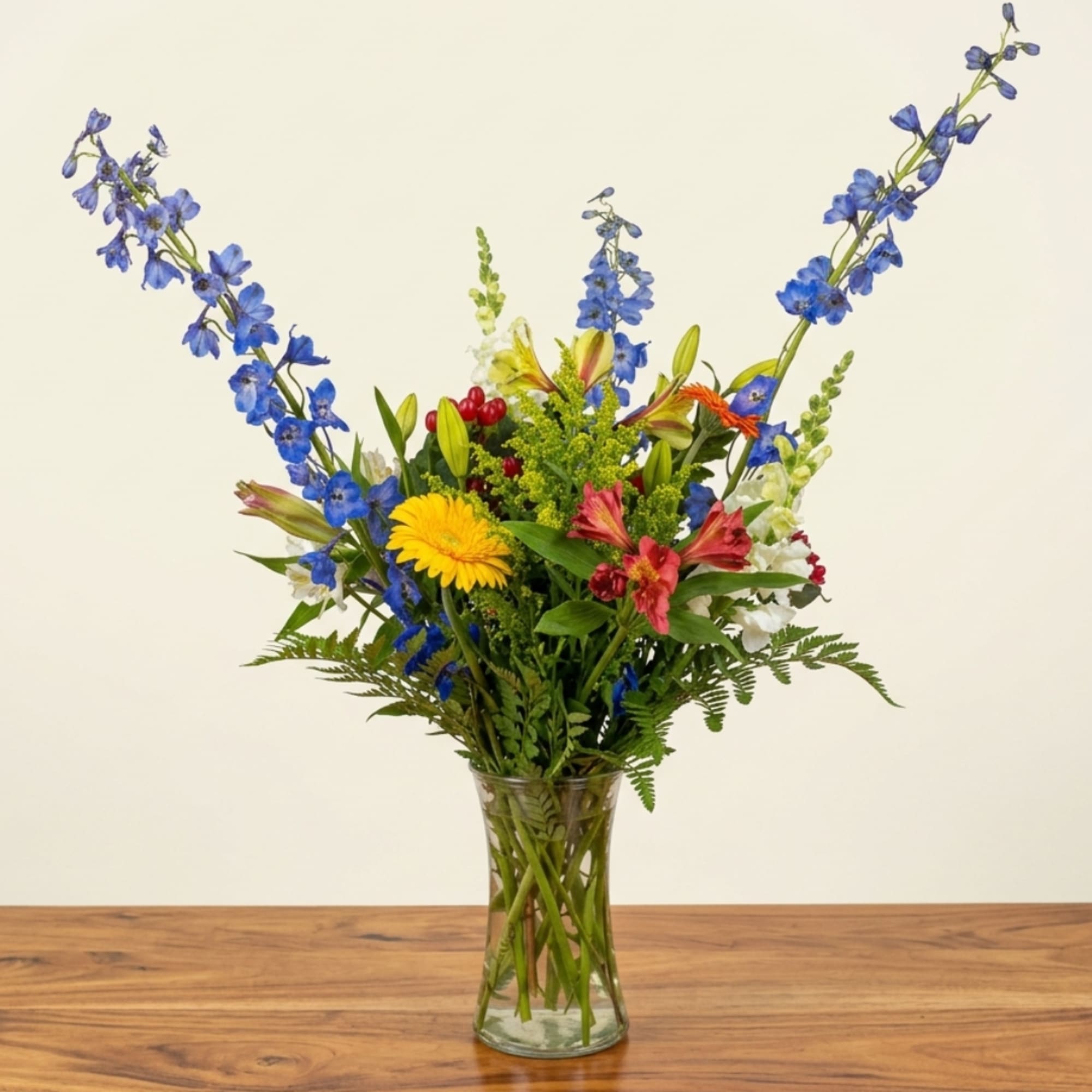 Mixed bouquet in a clear glass vase with blue, yellow, red, and white flowers