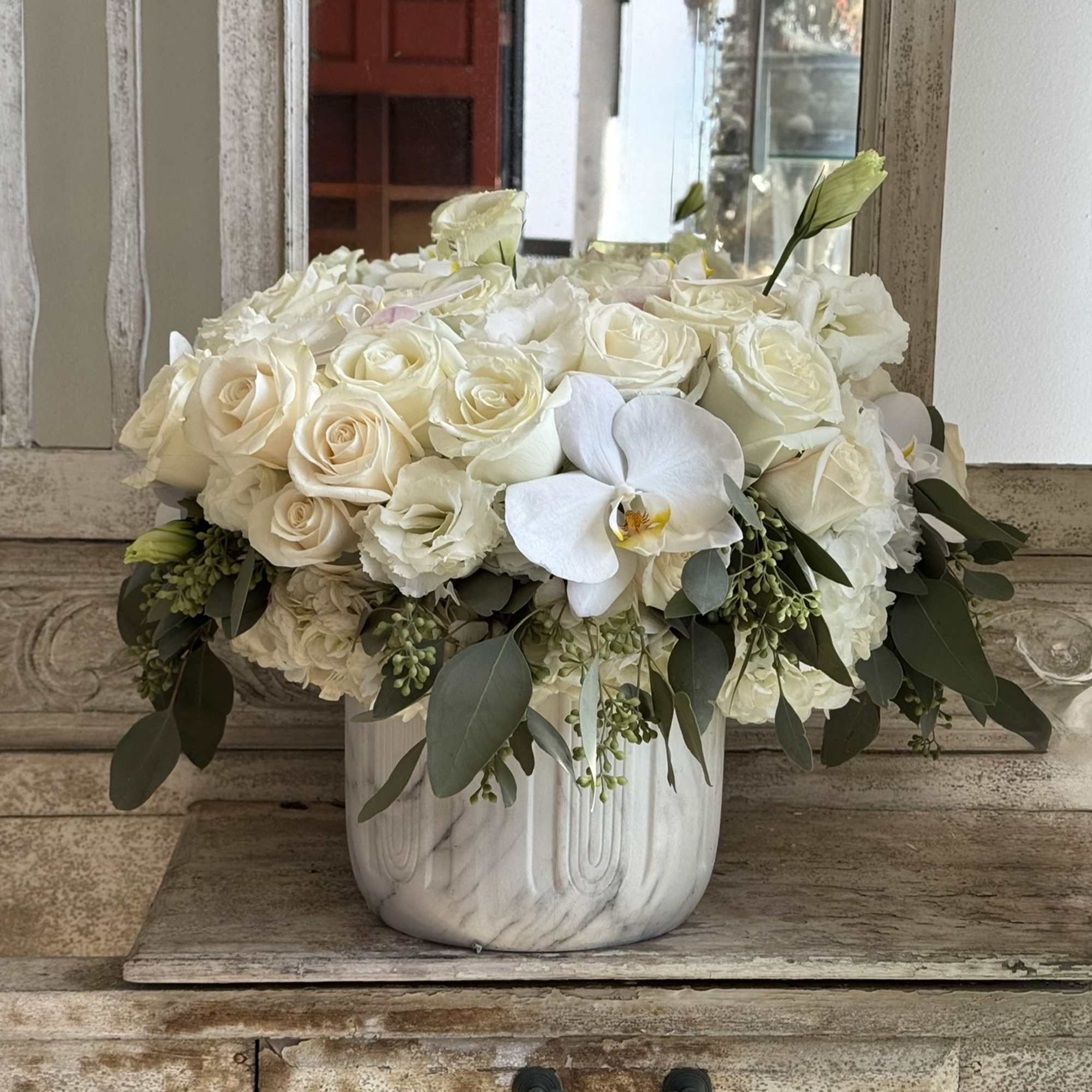 White rose arrangement in a marble-look vase with one white orchid bloom