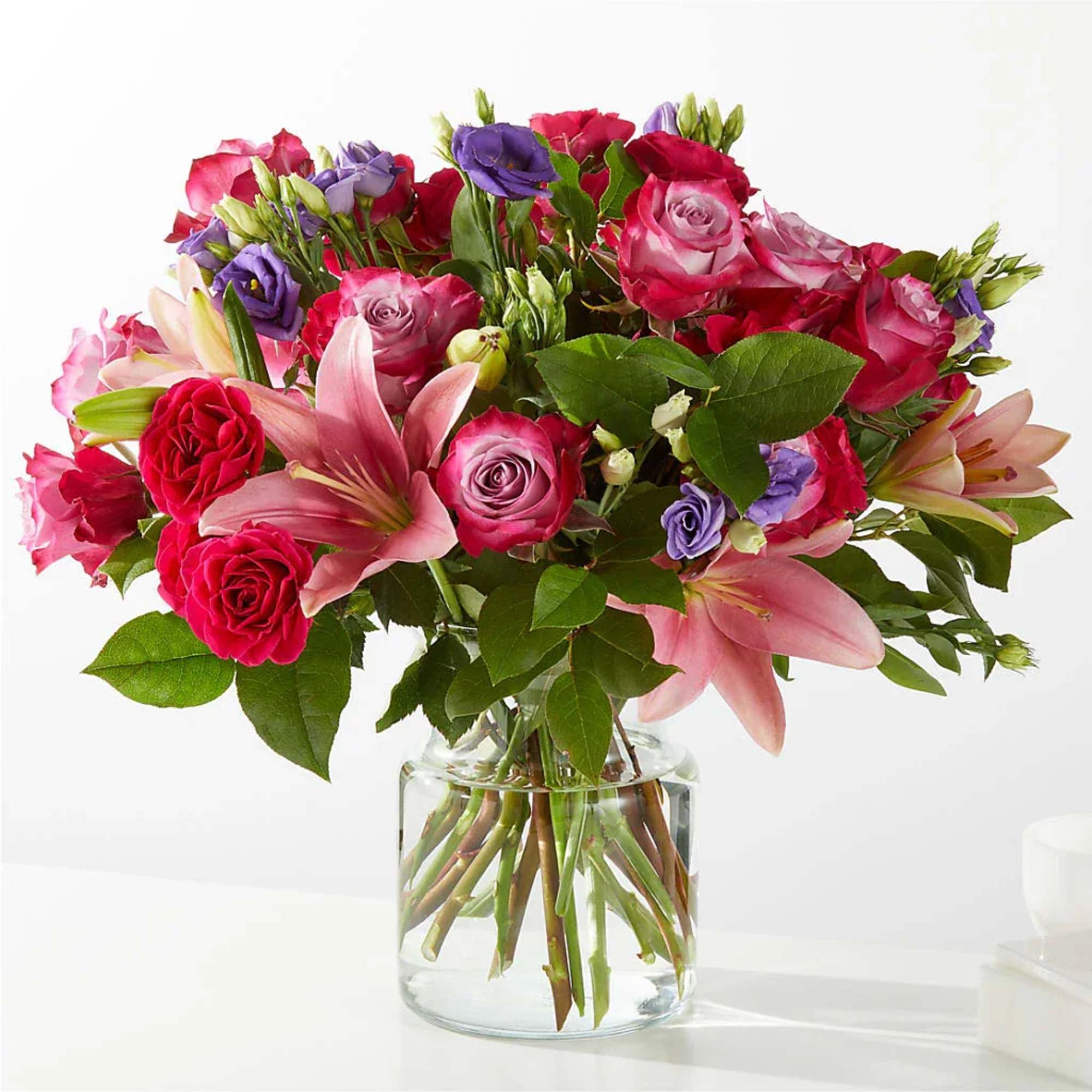Bouquet of pink roses, lilies, and purple blooms in a clear glass vase