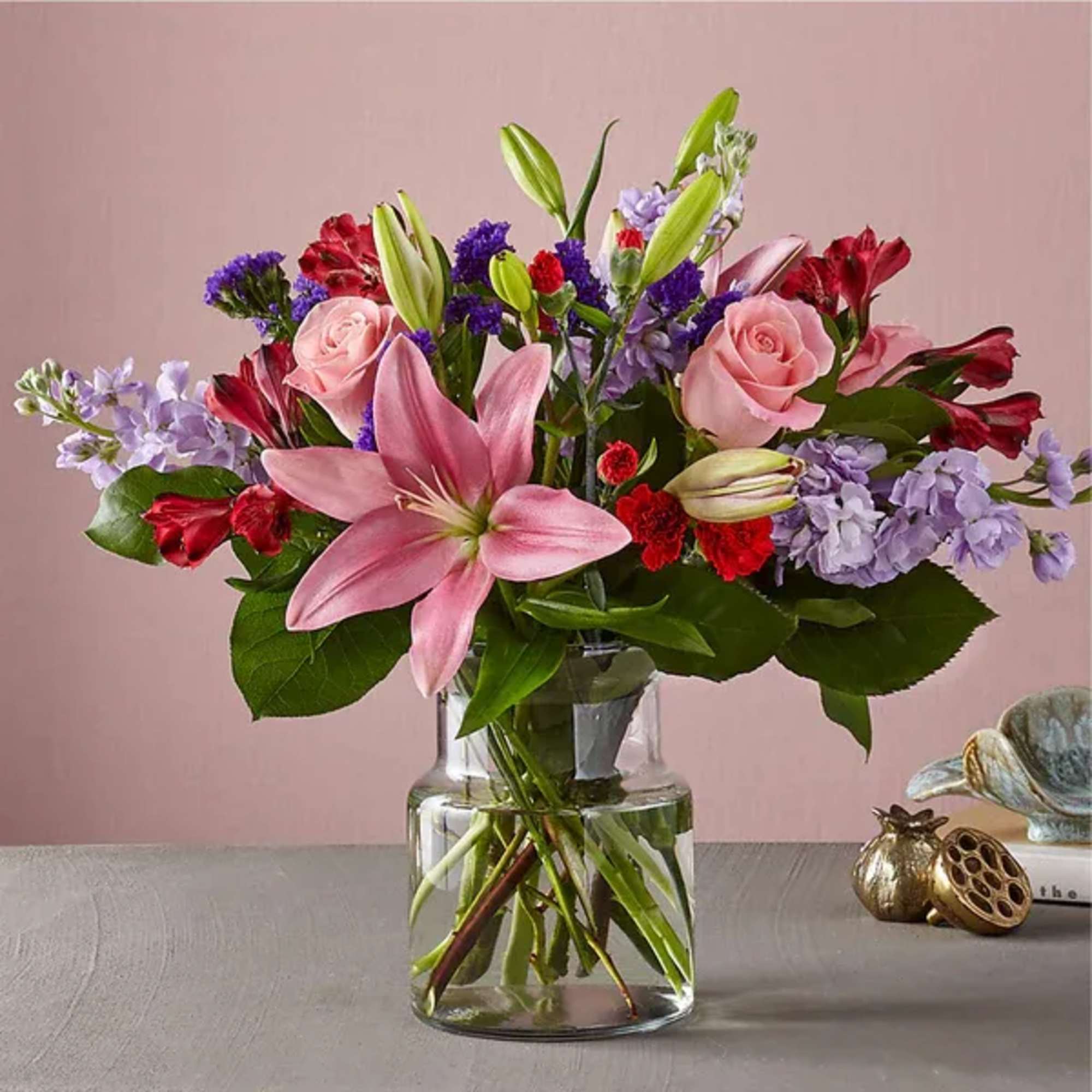 Pink lilies and roses in a clear glass vase with purple and red flowers