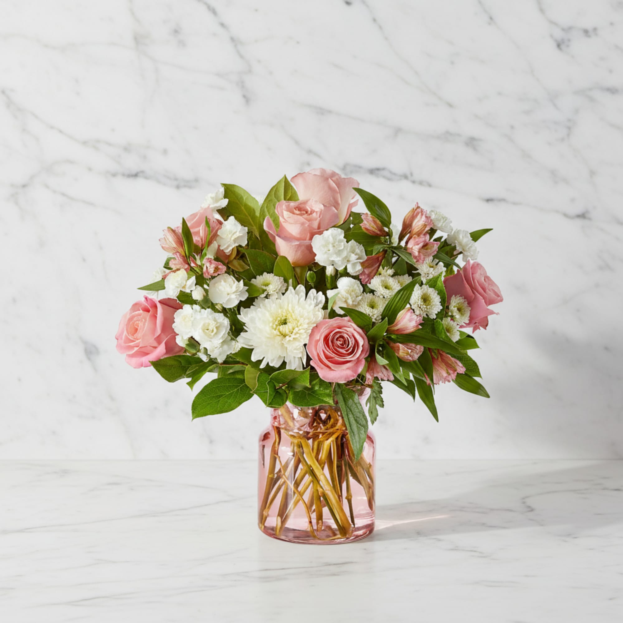 Pink roses and white flowers arranged in a pink glass vase
