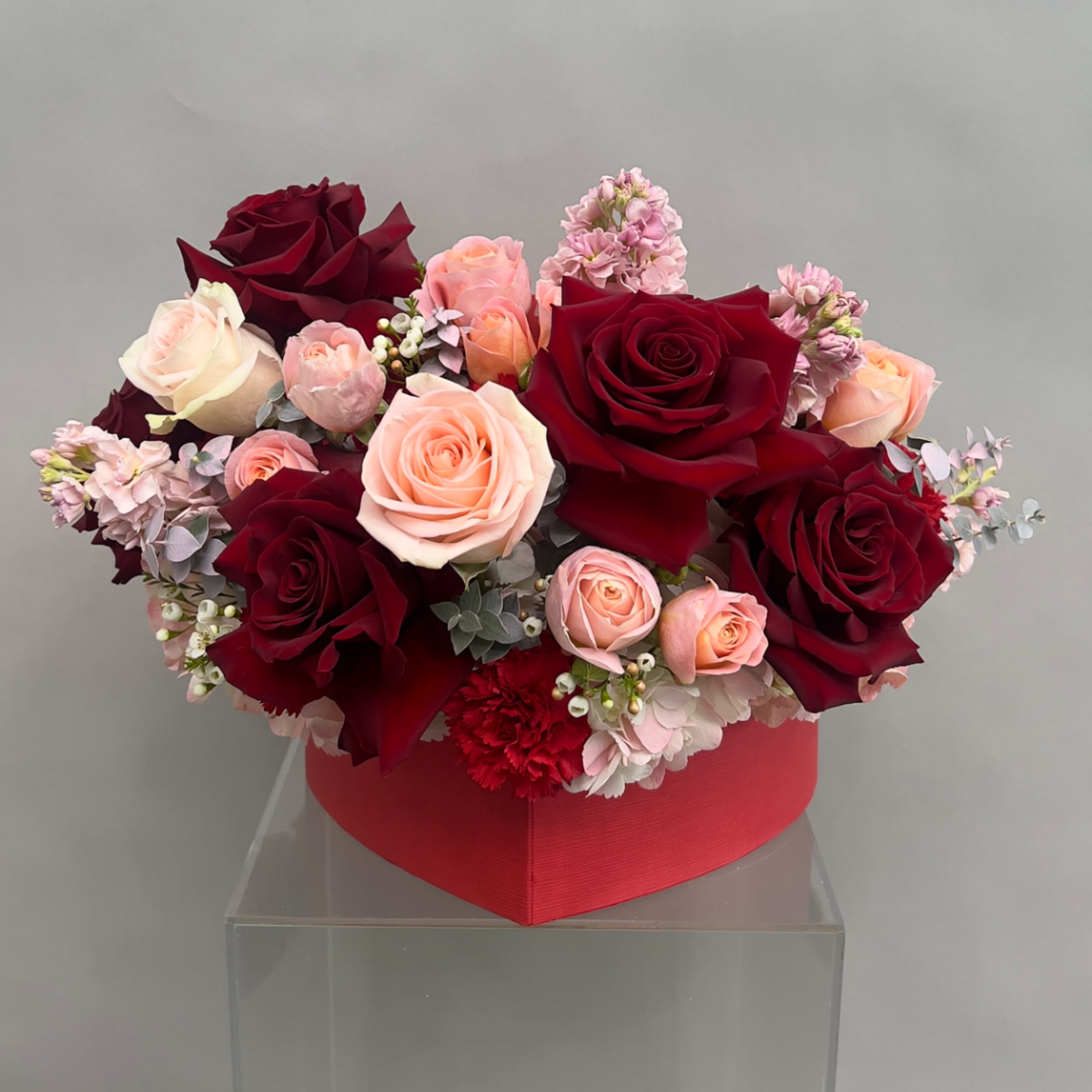 Heart-shaped box arrangement of red and blush roses with pink flowers