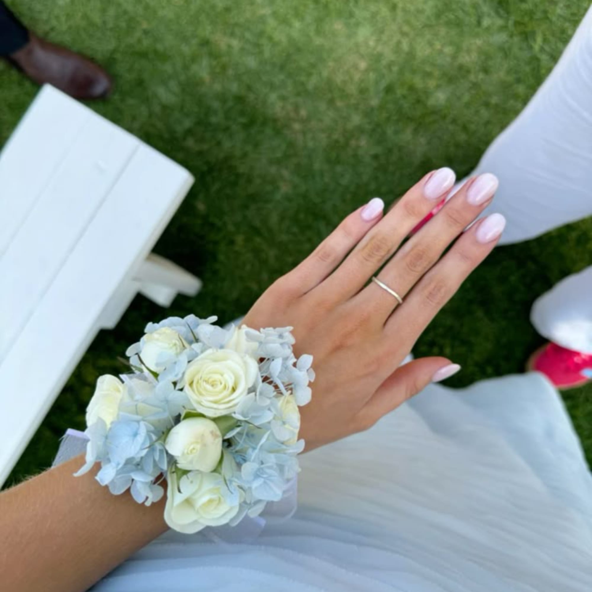 White rose wrist corsage with pale blue flowers on a hand