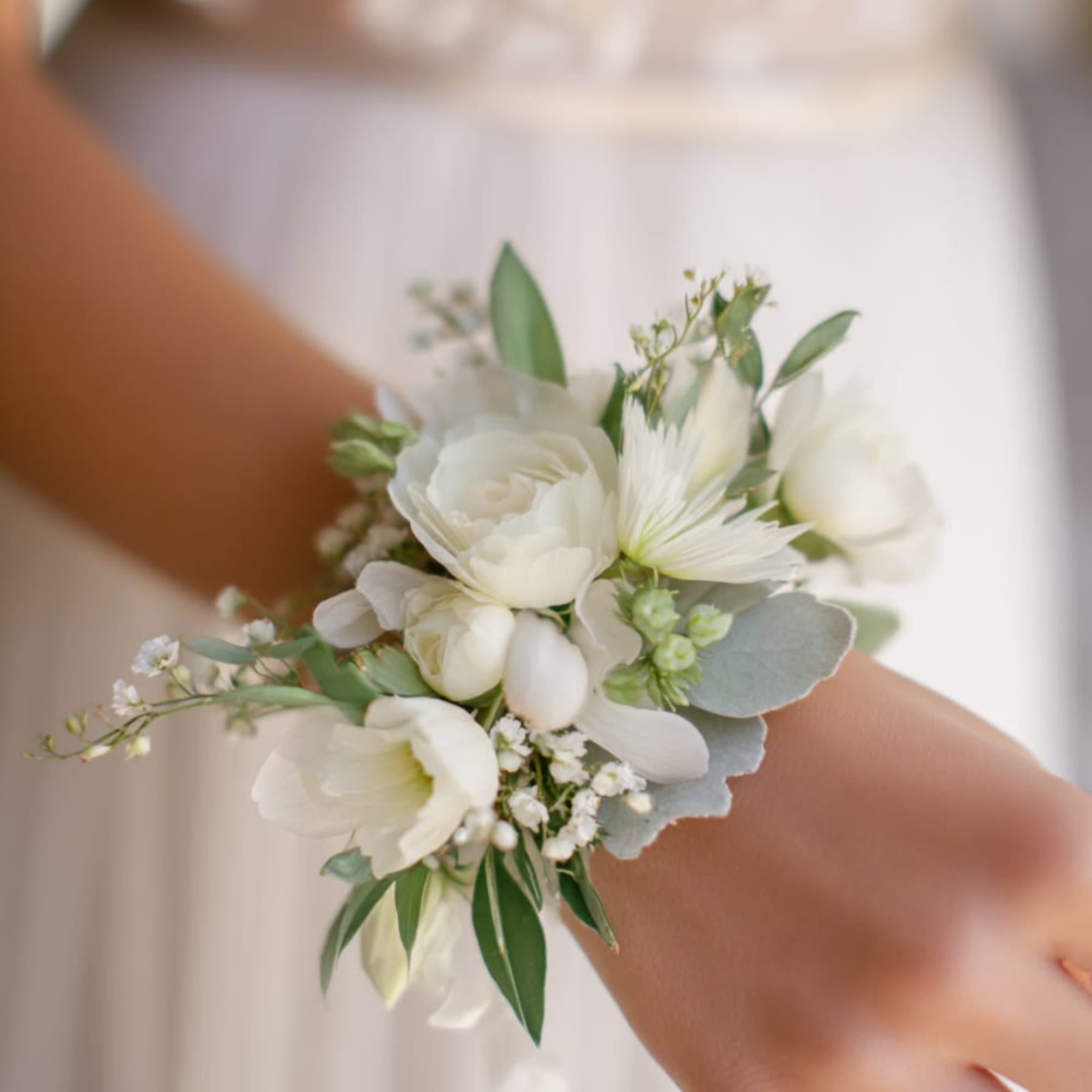 White floral wrist corsage with soft greenery on a person’s wrist