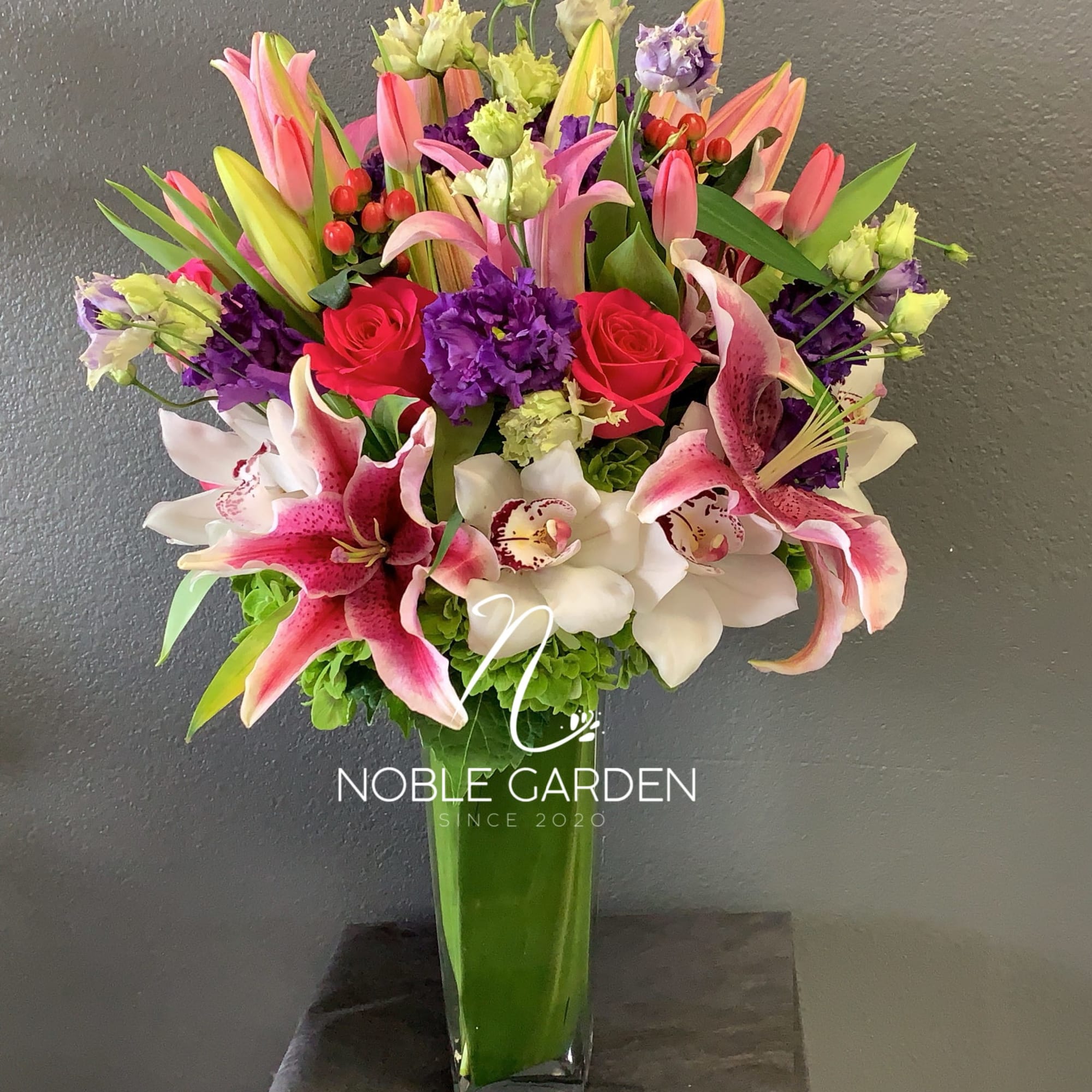 Tall bouquet of pink lilies, roses, and orchids in a glass vase