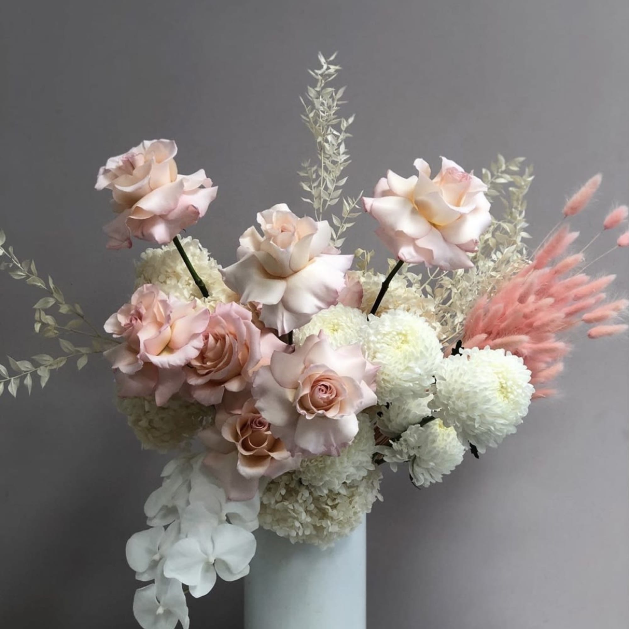 Pink roses and white pompom flowers in a tall white vase