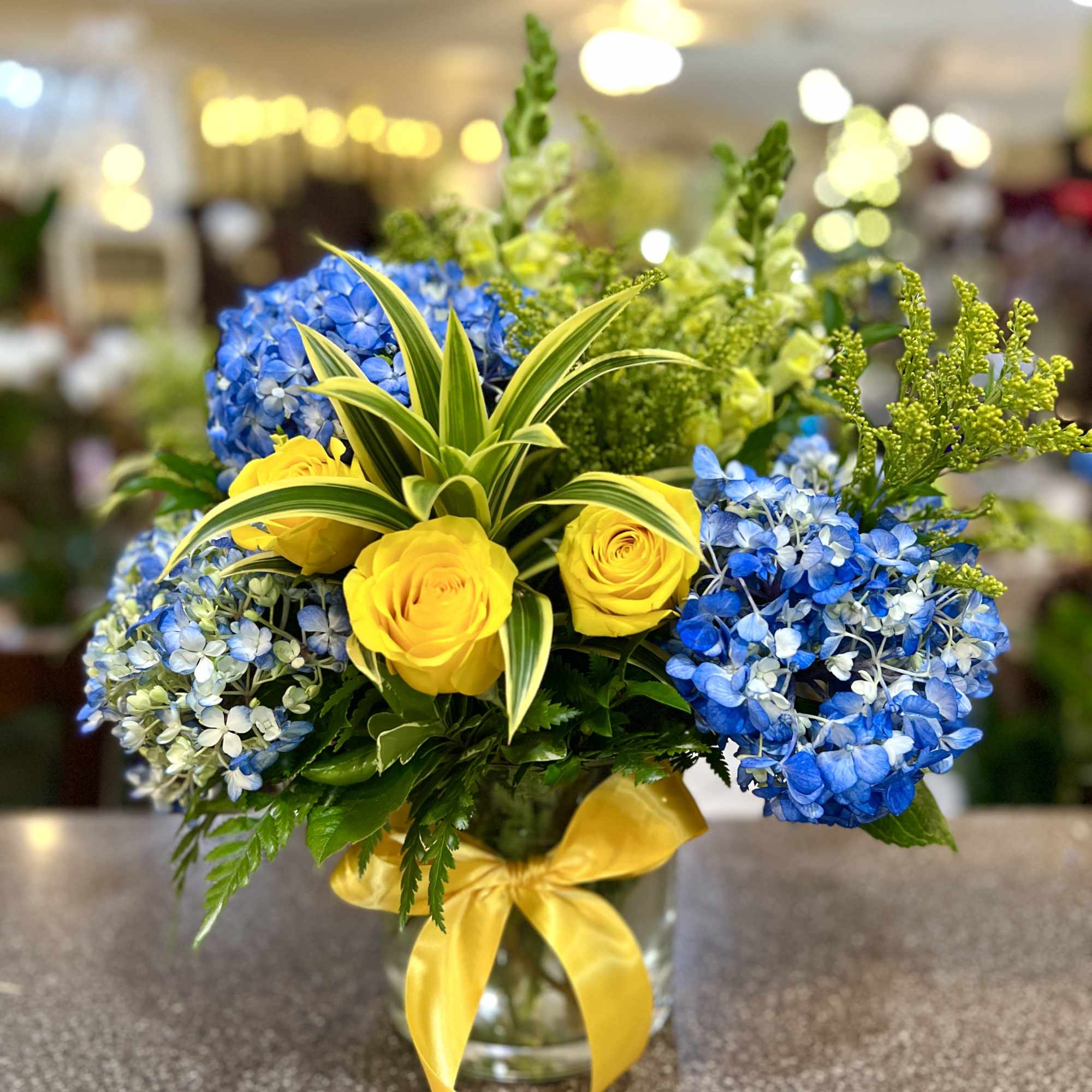 Blue hydrangeas and yellow roses in a glass vase with a yellow ribbon, photo 2 of 2