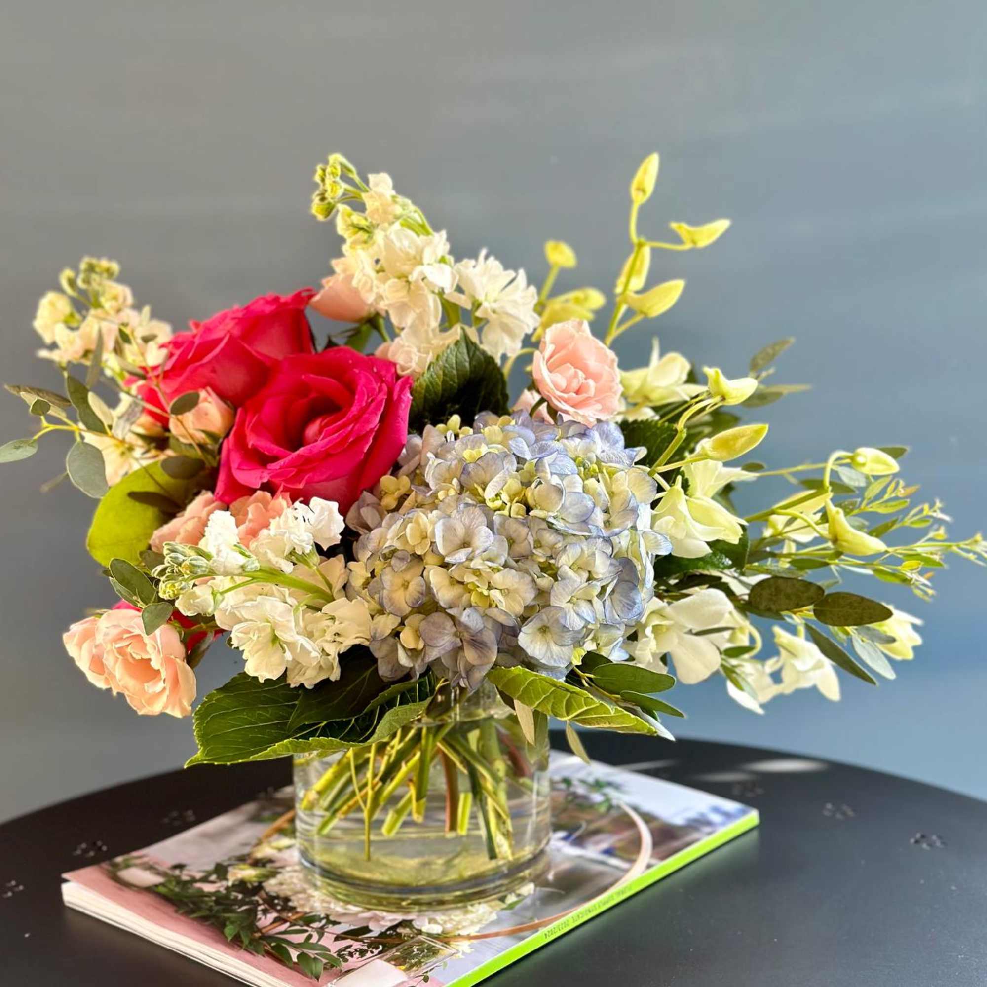 Bouquet of pink roses, blue hydrangea, and white flowers in a glass vase