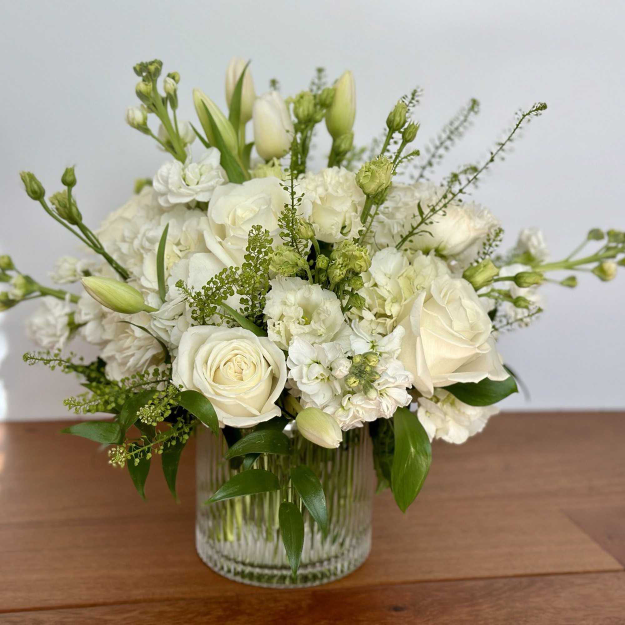 White roses and mixed white flowers in a clear glass vase