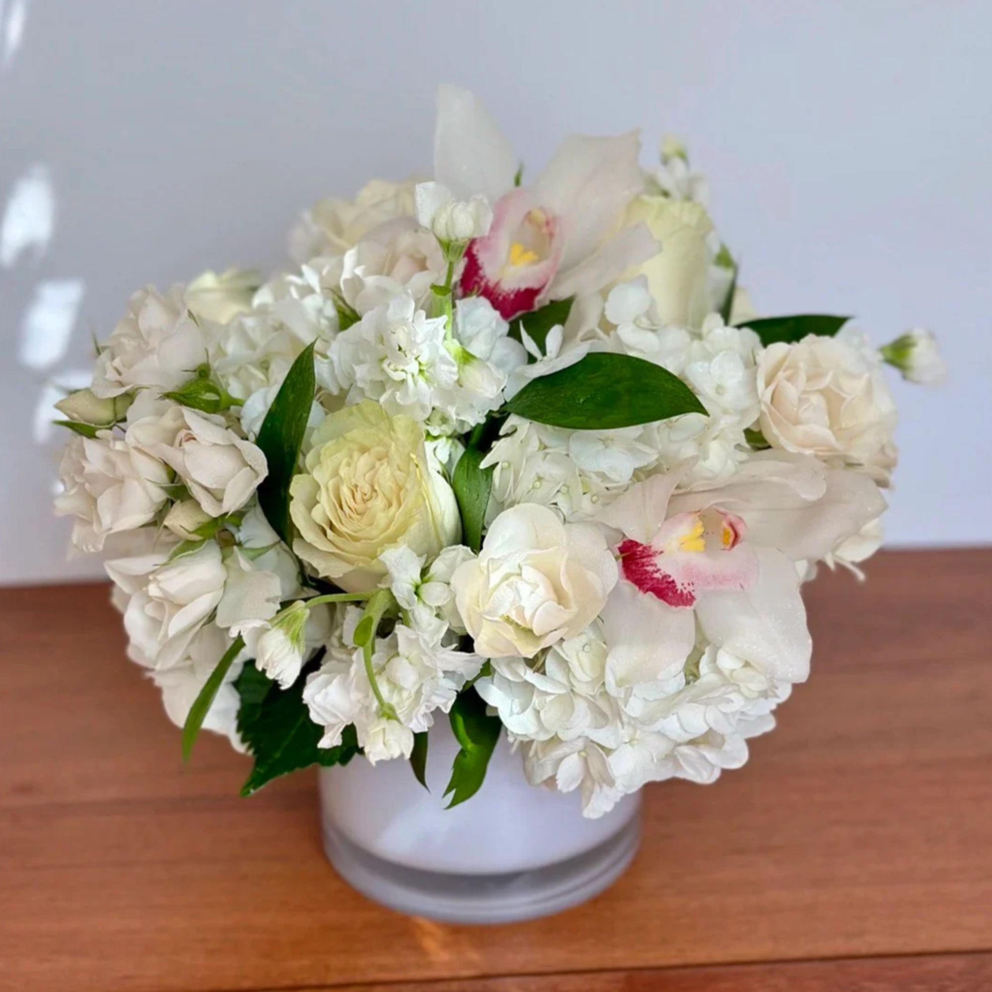 White floral arrangement in a round vase with pale roses and orchids