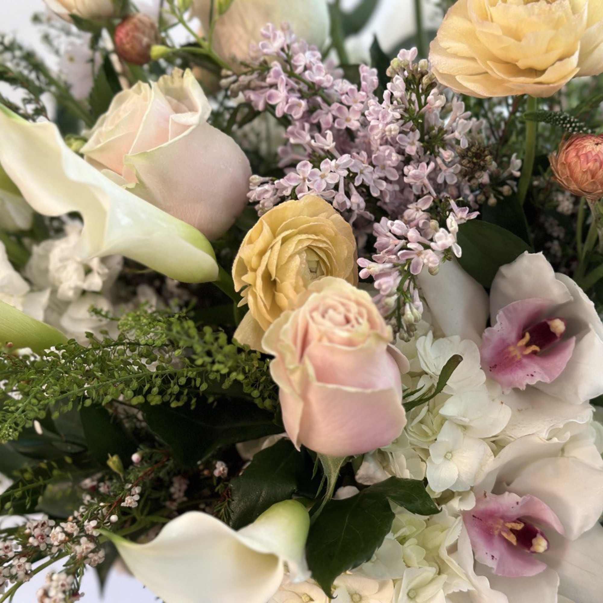 Pastel bouquet with calla lilies, roses, ranunculus, lilac, orchids, and hydrangeas in peach, pink, and white.