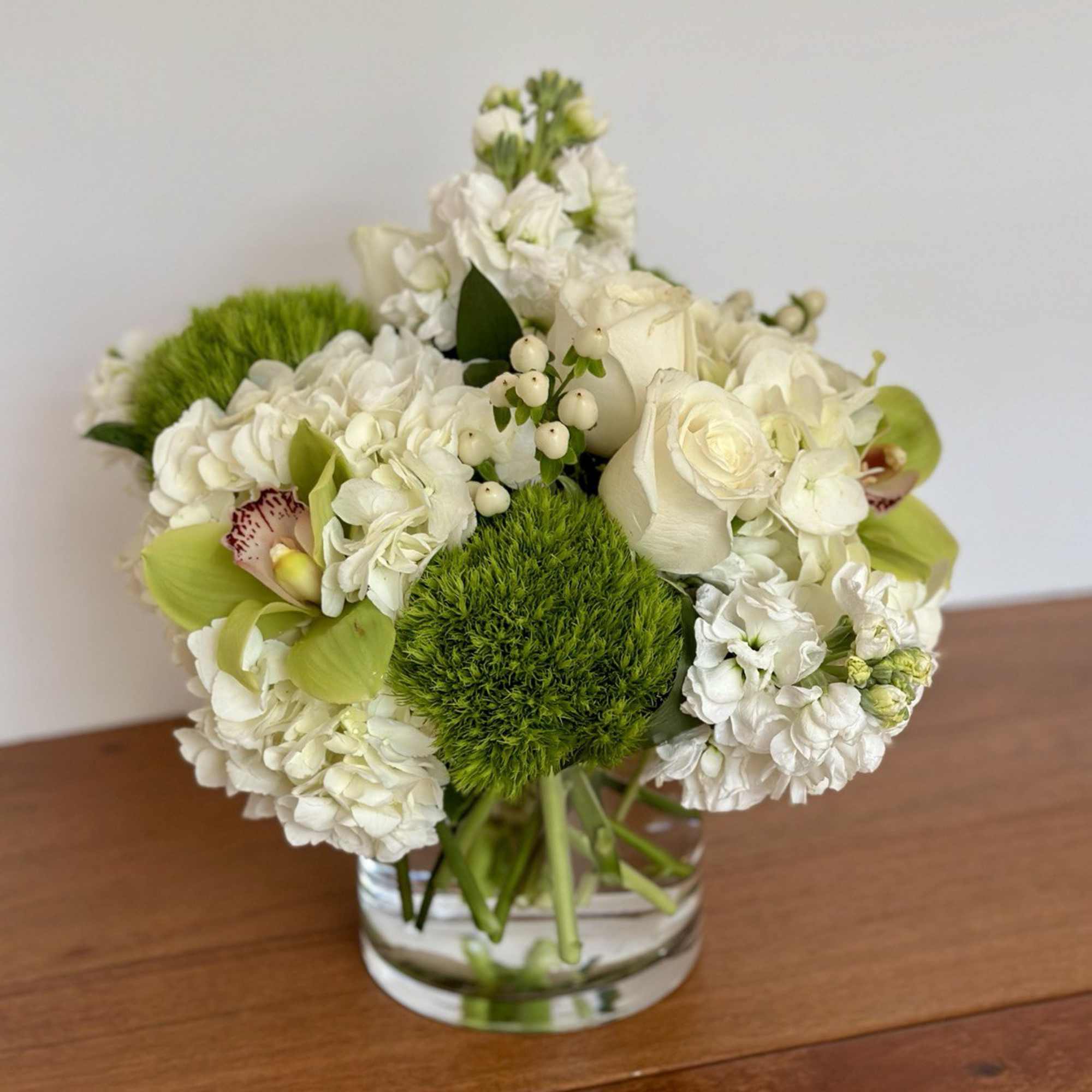 White floral arrangement in a clear glass vase with green accents