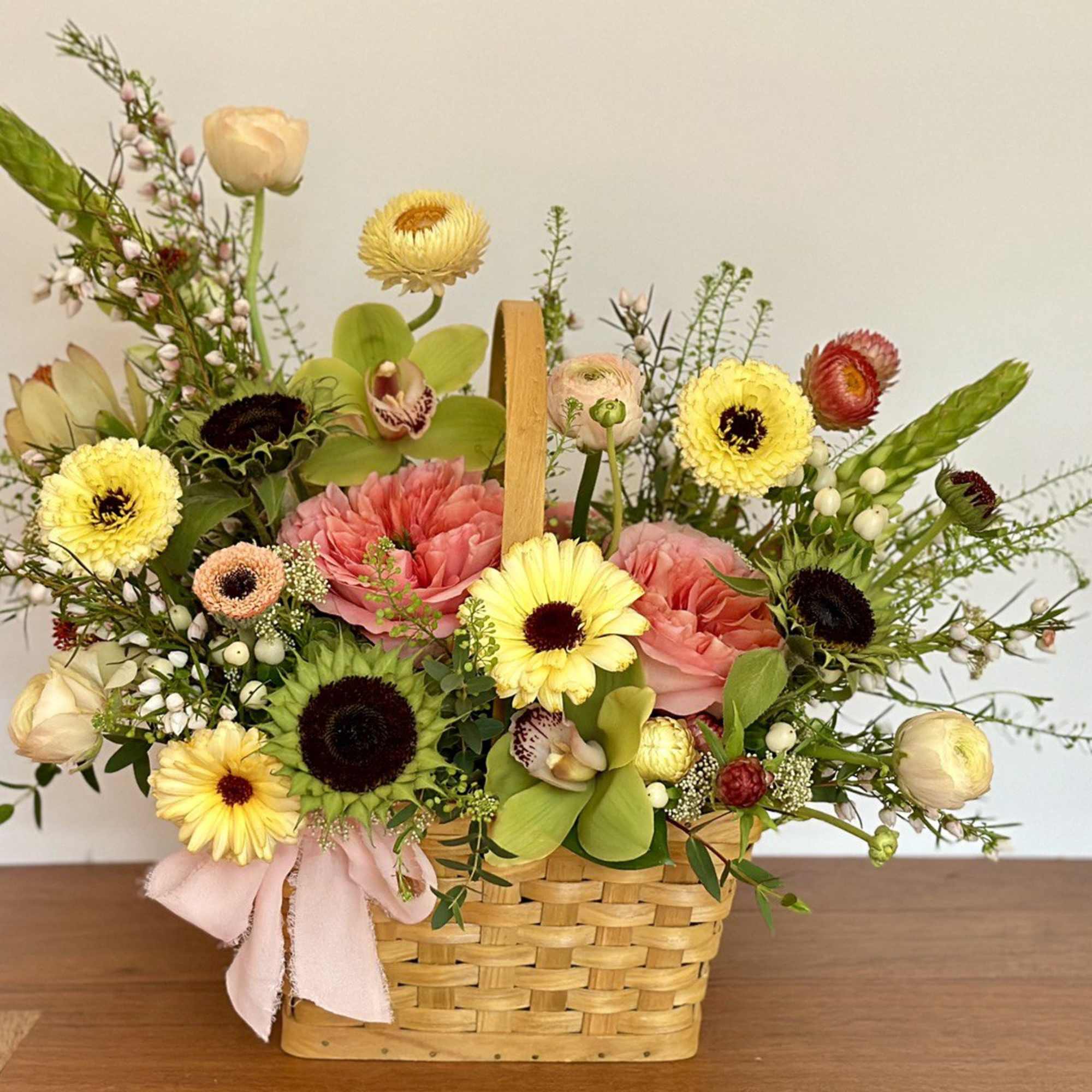Mixed flower arrangement in a woven basket with a pink ribbon
