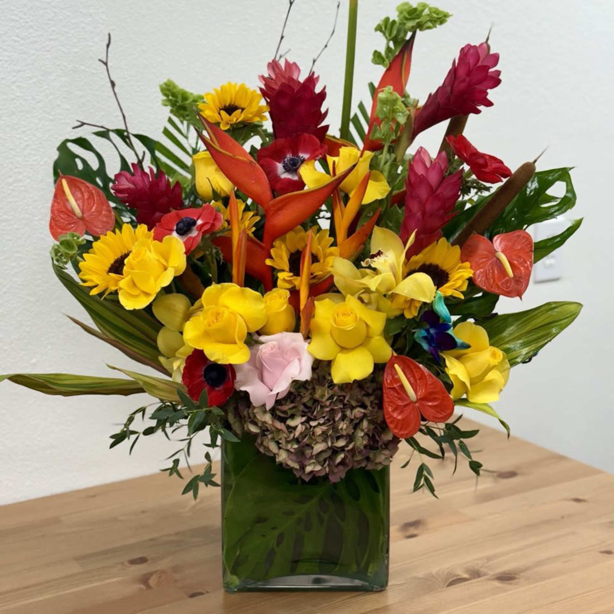 Tropical bouquet with yellow sunflowers and red-orange blooms in a green vase