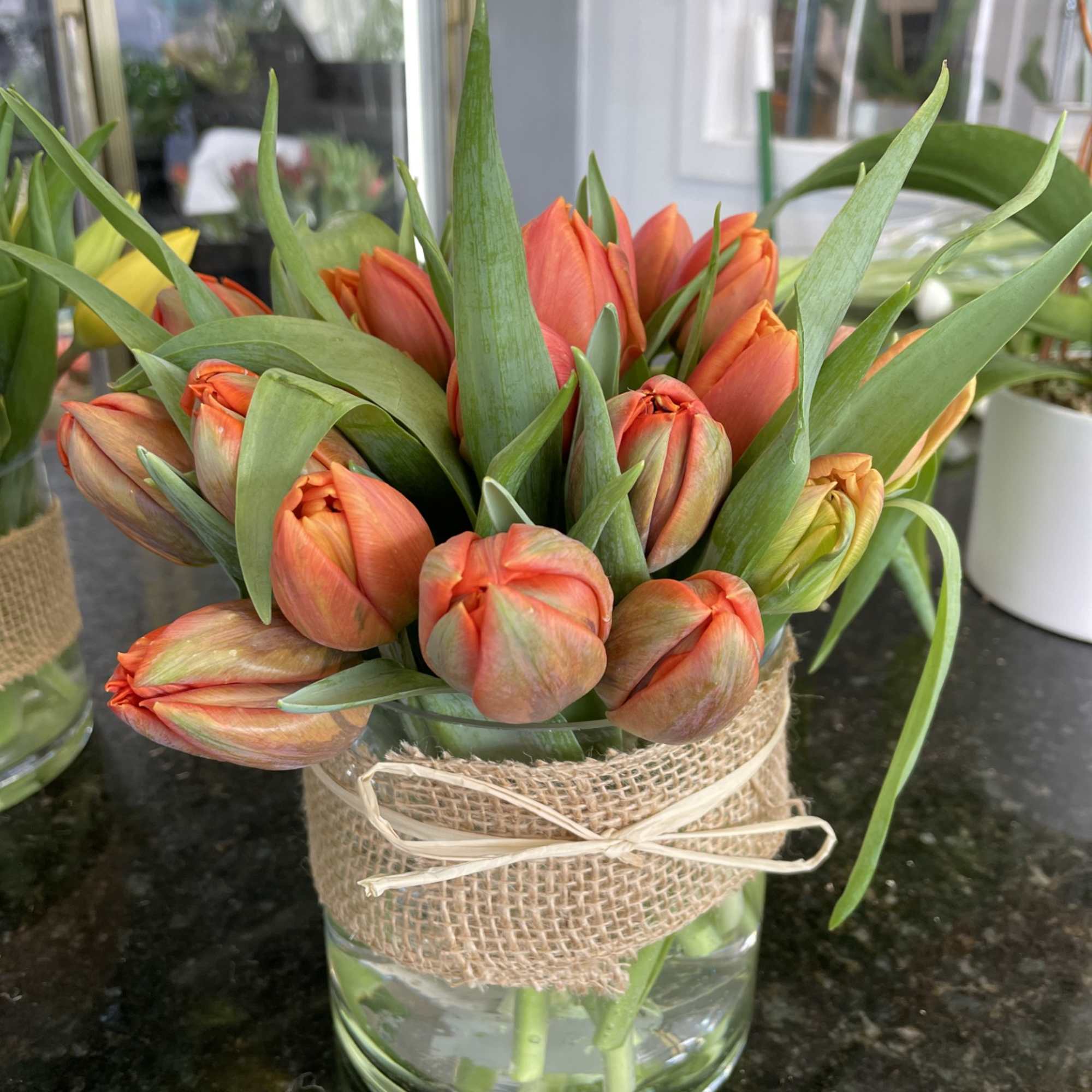 Orange tulip bouquet in a glass vase wrapped with burlap and ribbon