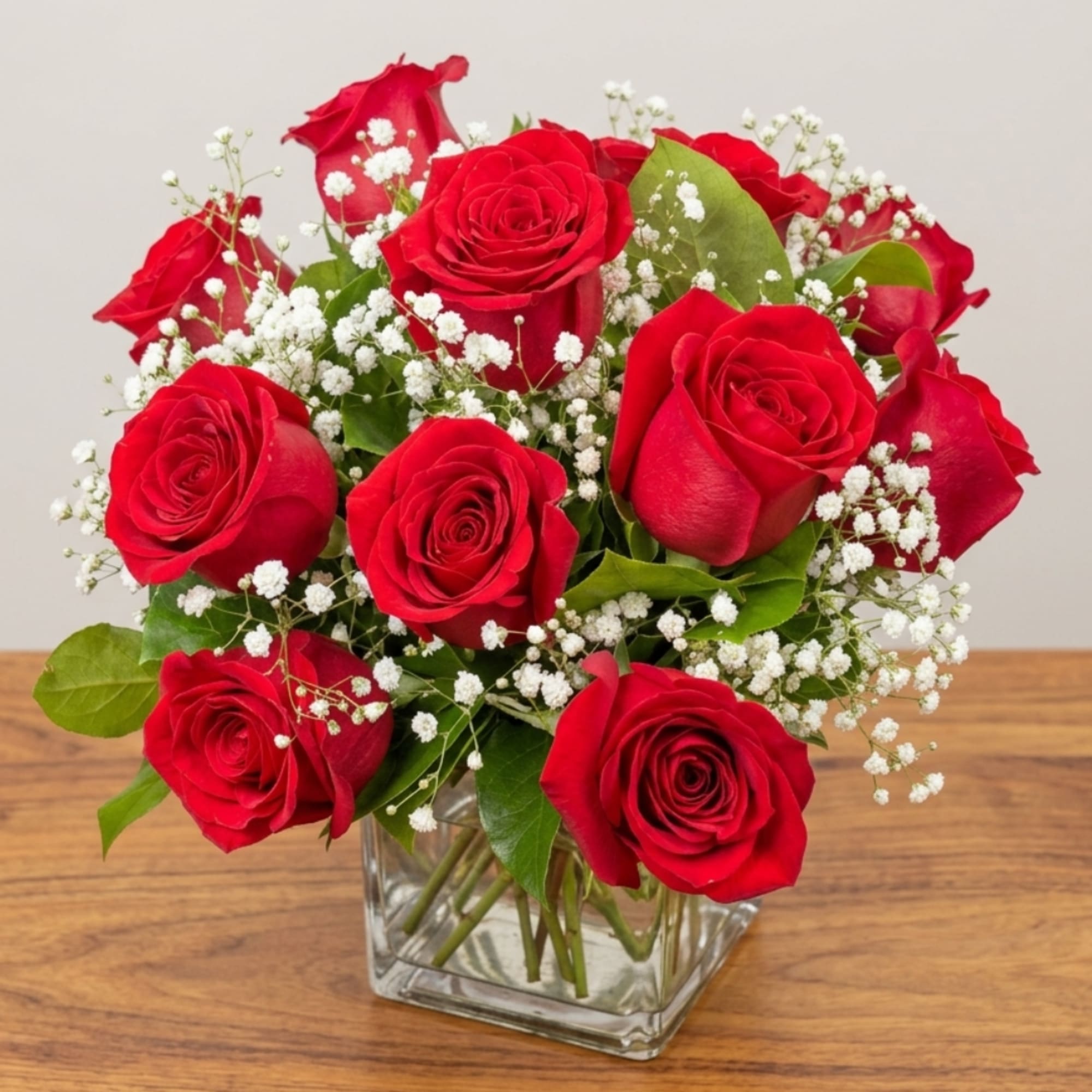 Red roses arranged in a clear square vase with white filler flowers