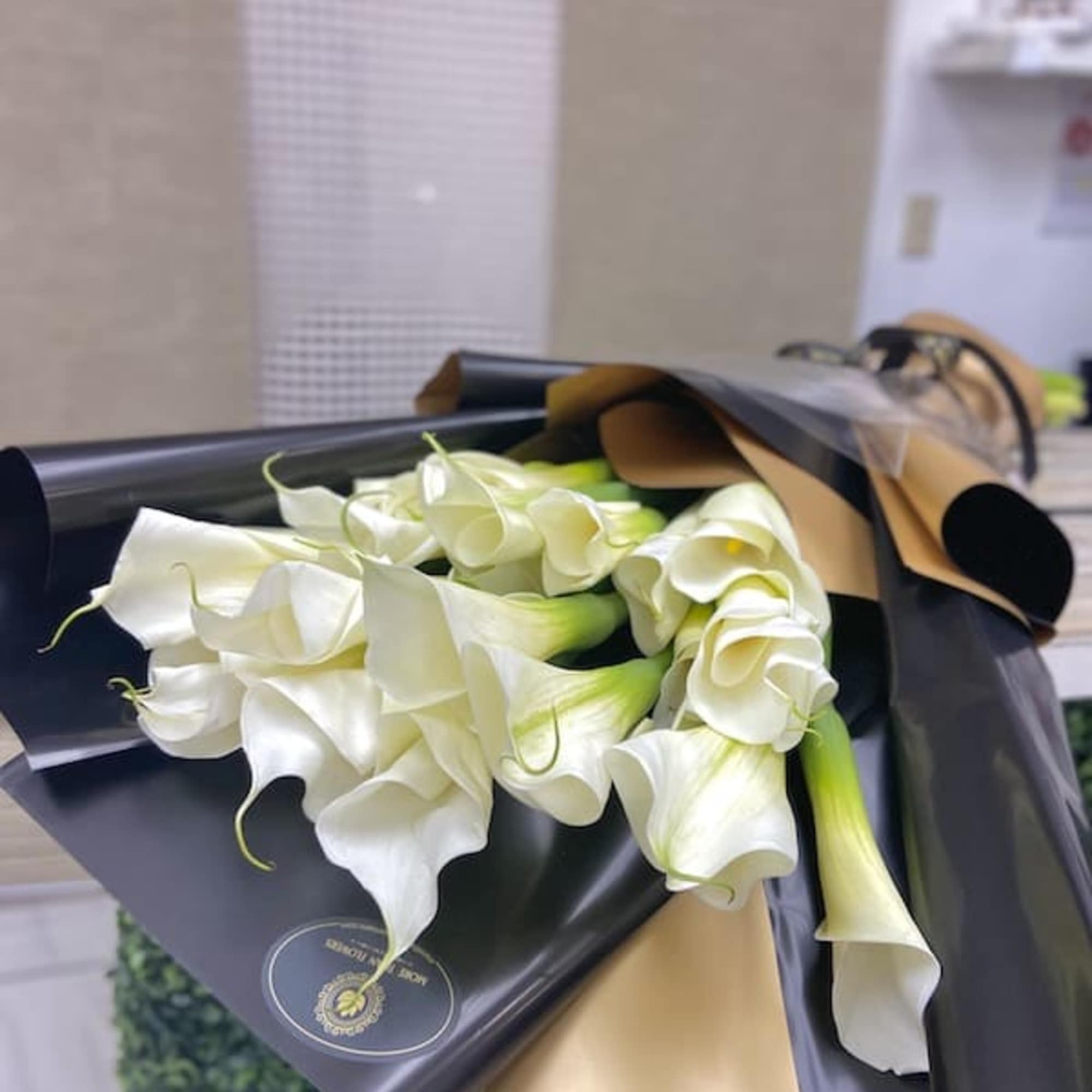 Wrapped bouquet of white calla lilies in black and gold paper on a countertop.