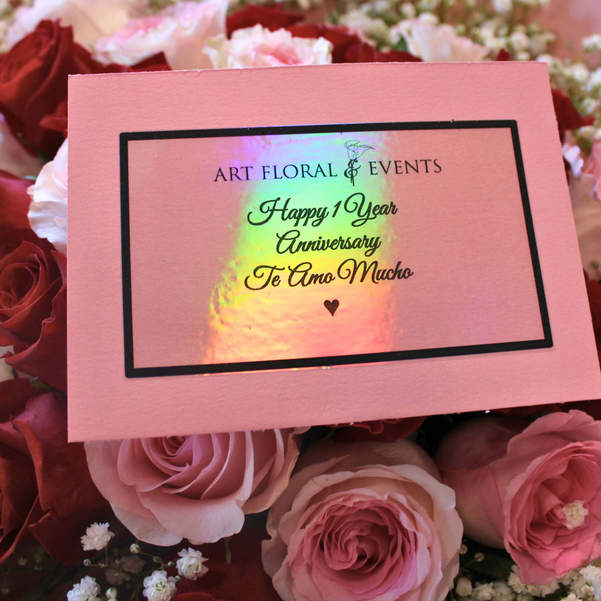 Pink and red roses arranged around a pink anniversary card