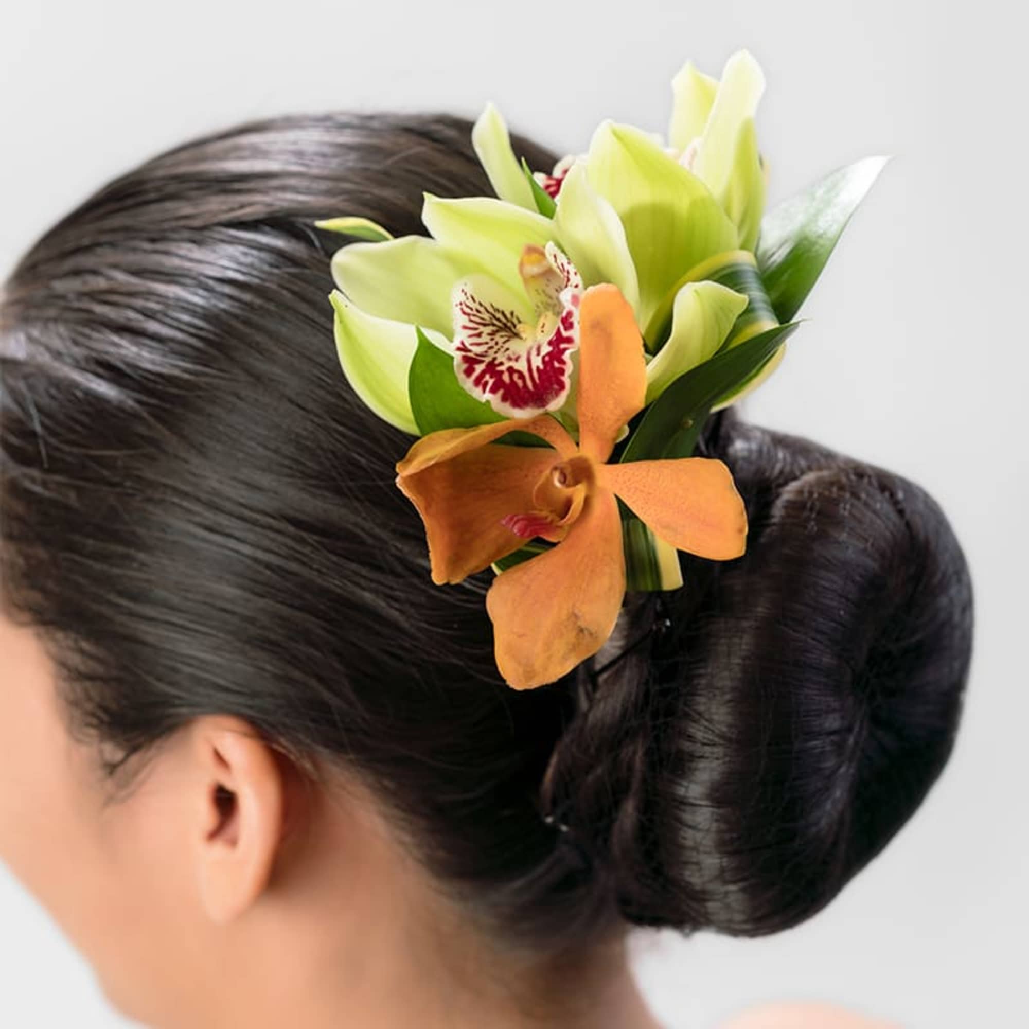 Floral hairpiece with green and orange orchids pinned into a sleek dark hair bun.