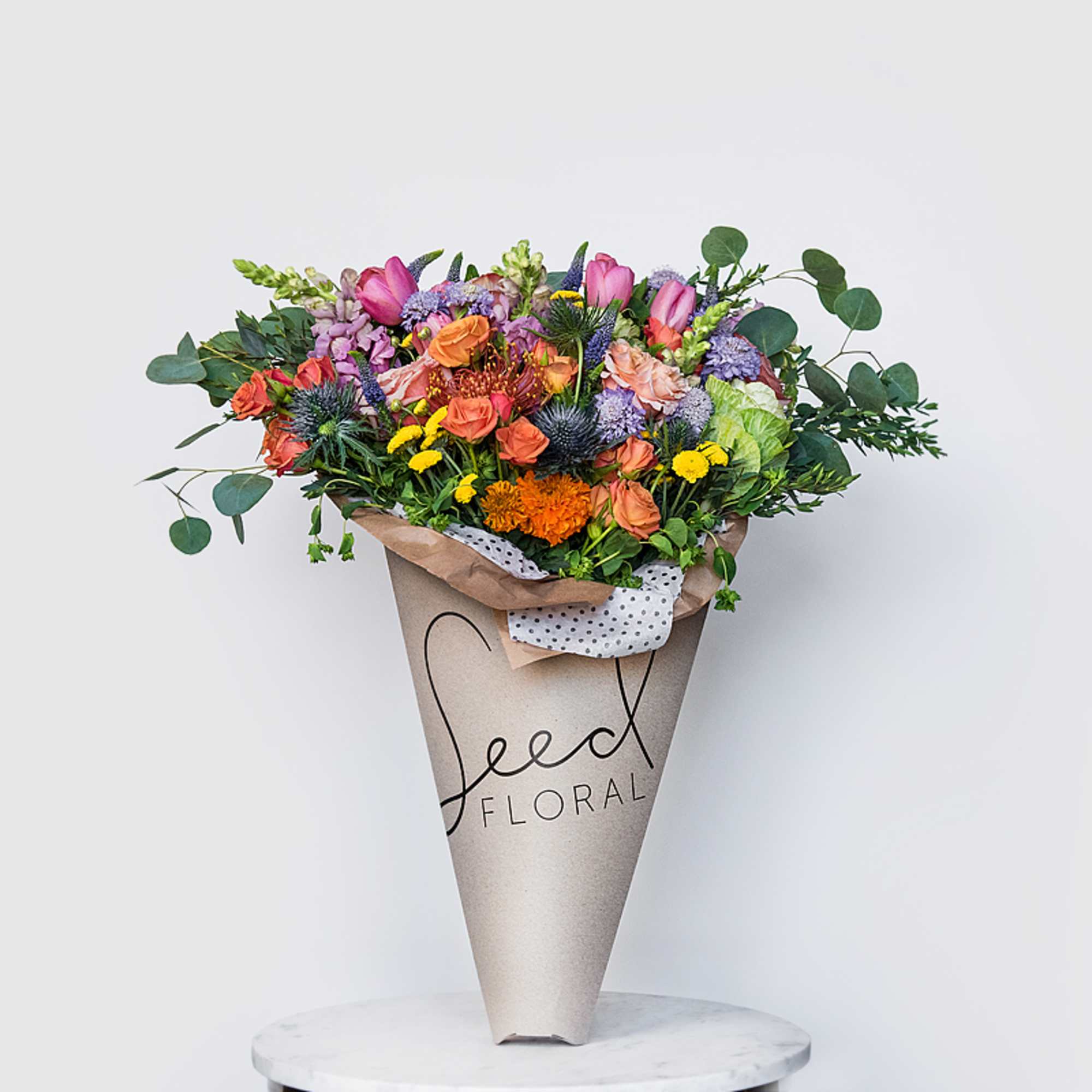 Bright mixed bouquet of pink tulips, orange roses, and colorful blooms in a kraft paper cone wrap