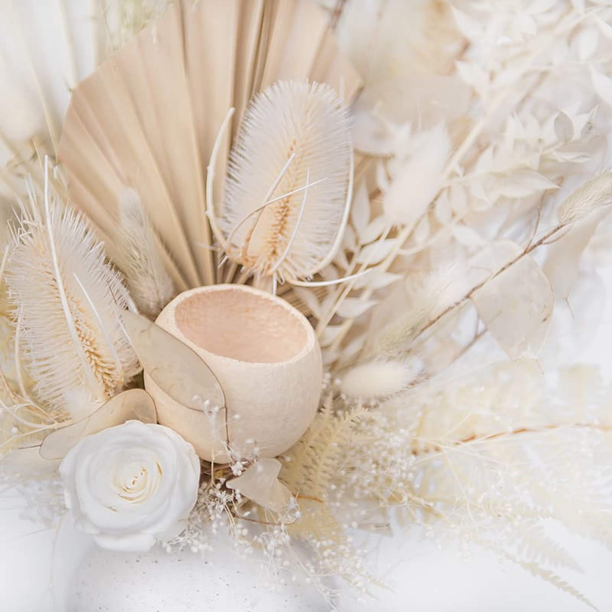 Cream-toned floral arrangement with a white rose and dried palm accents