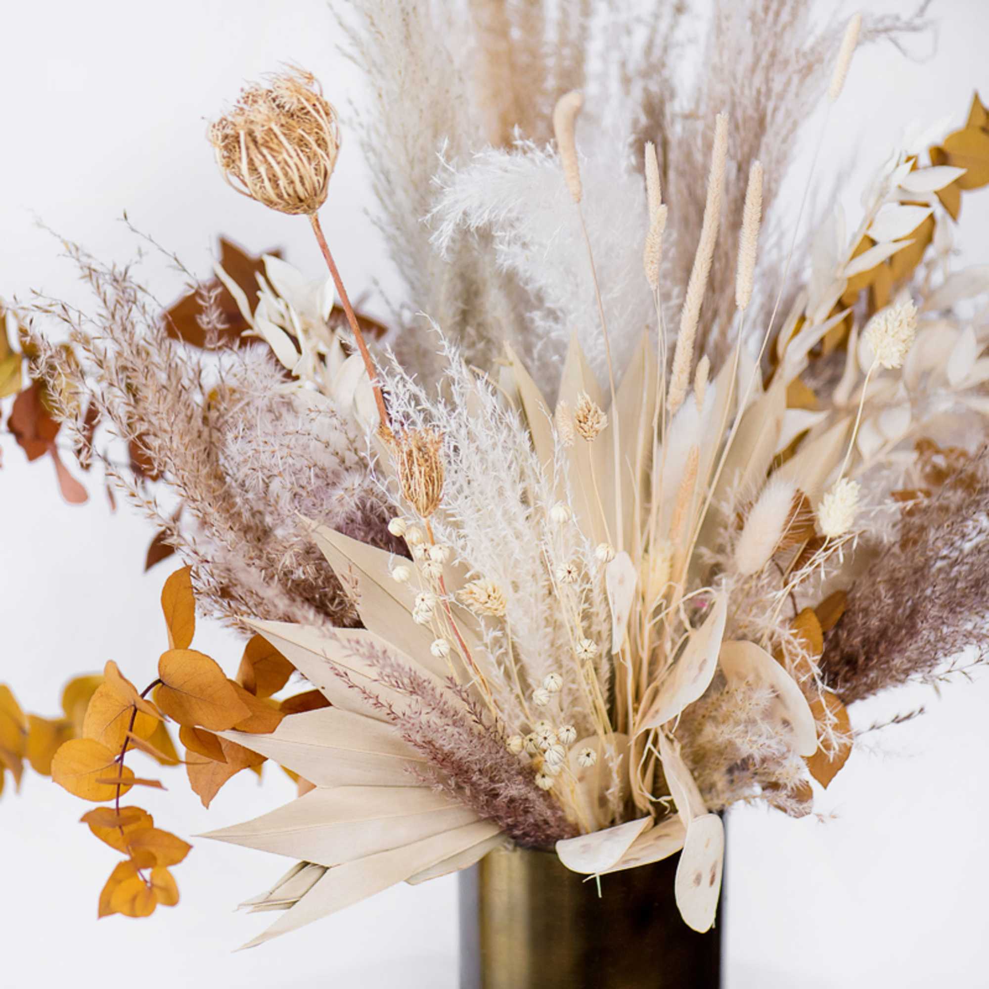 Dried floral arrangement in a gold vase with beige and white textures