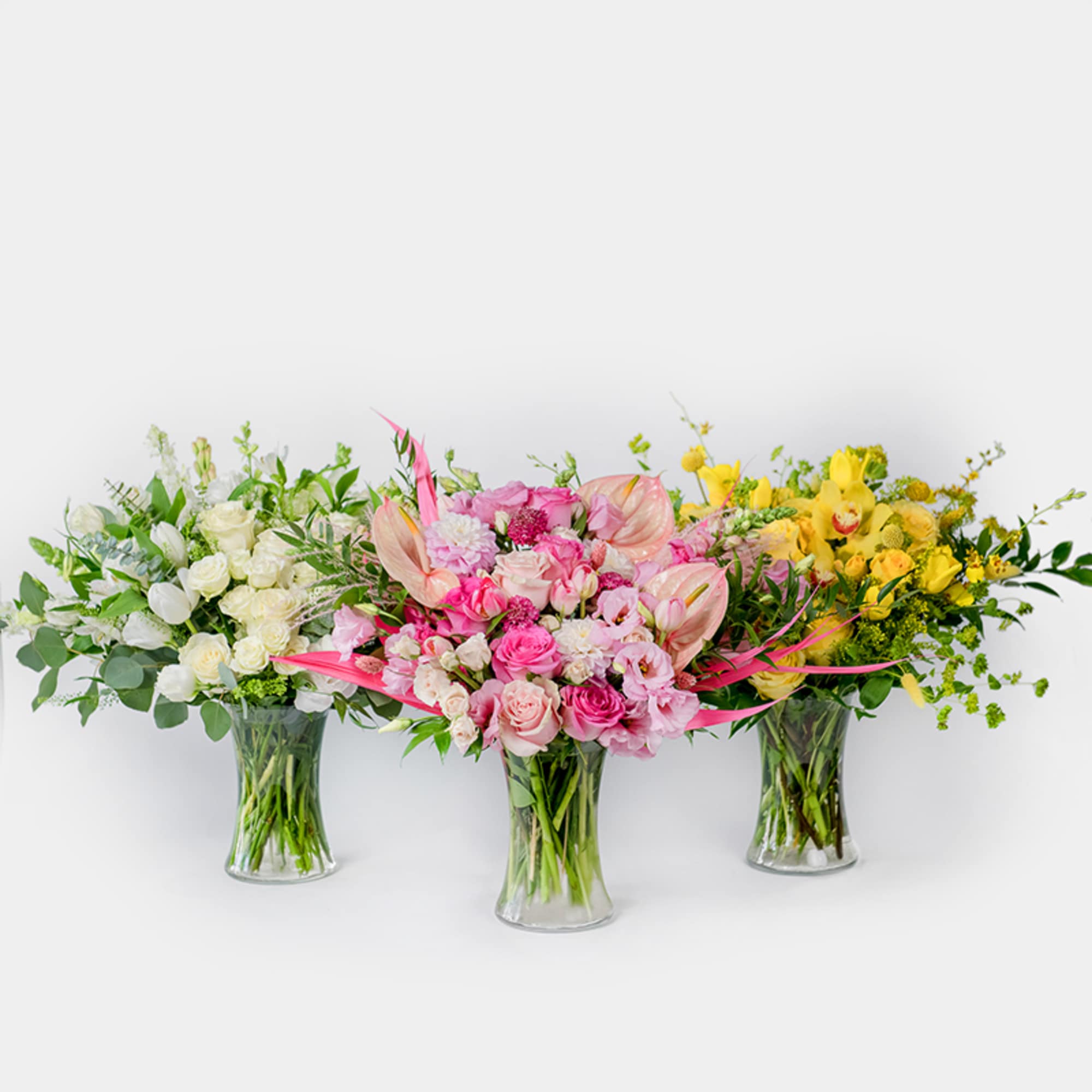 Three colorful floral arrangements in clear glass vases
