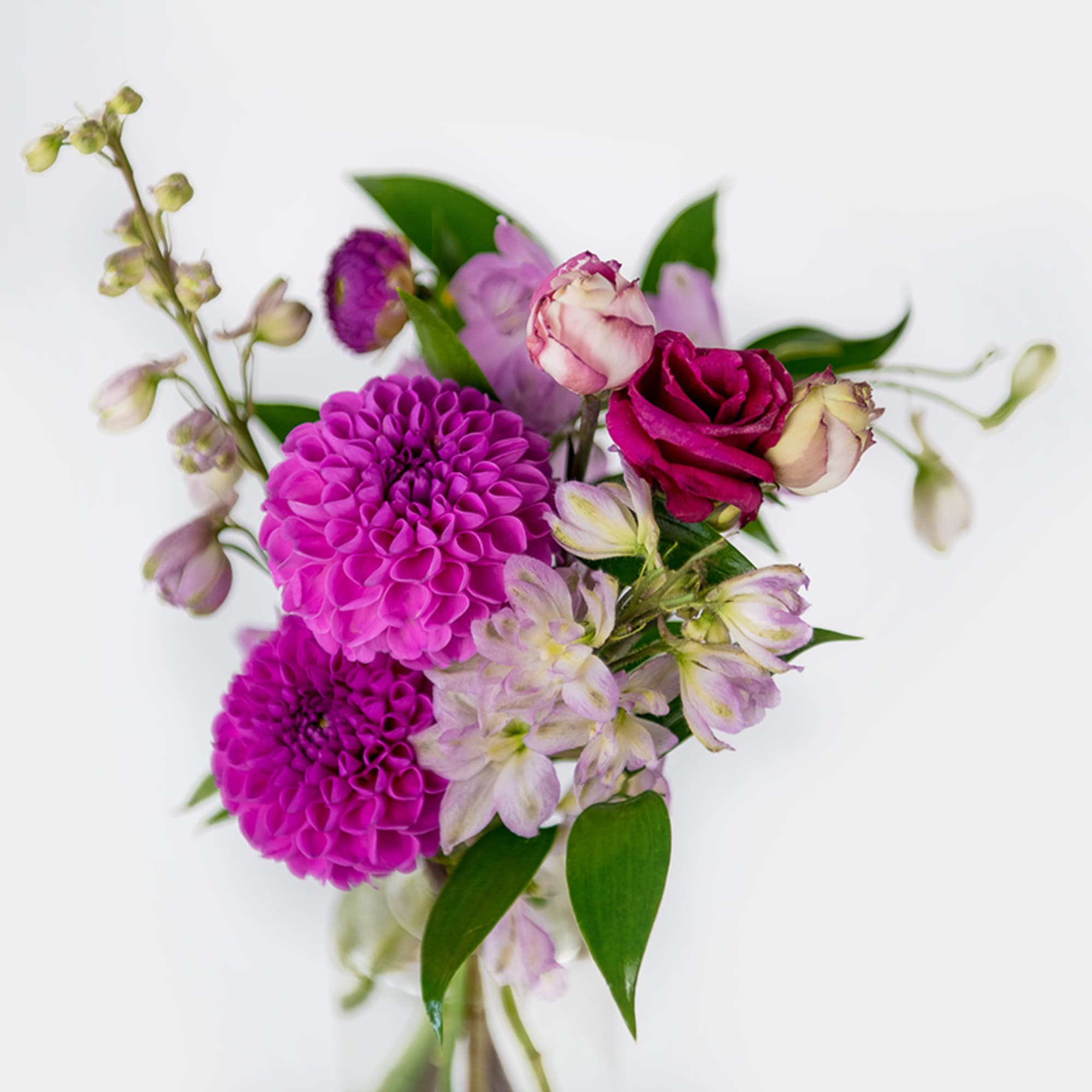 Small bouquet of bright magenta dahlias and pink roses with pale blooms in a clear glass vase