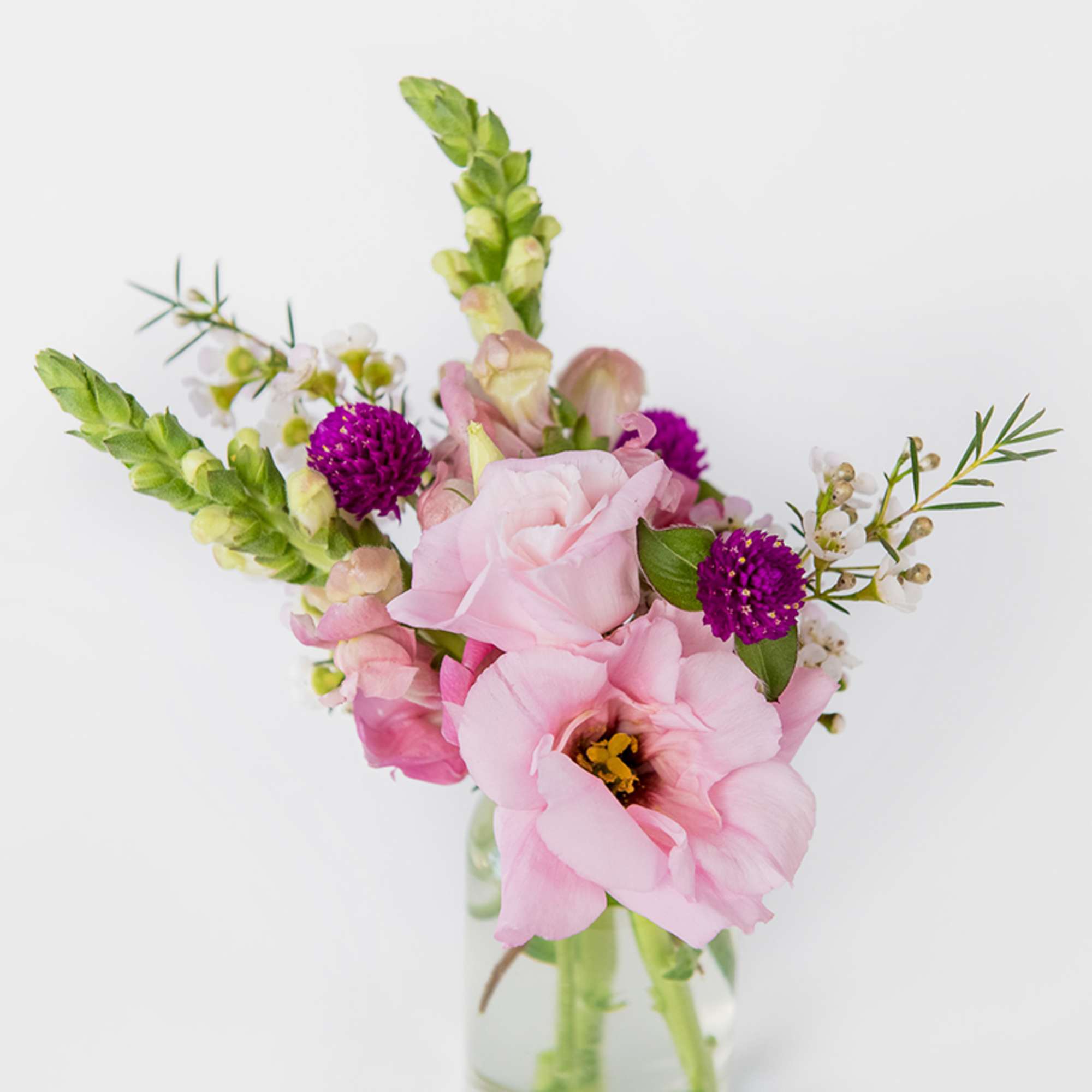 Small arrangement of pink lisianthus and snapdragons with purple accents in a clear glass vase