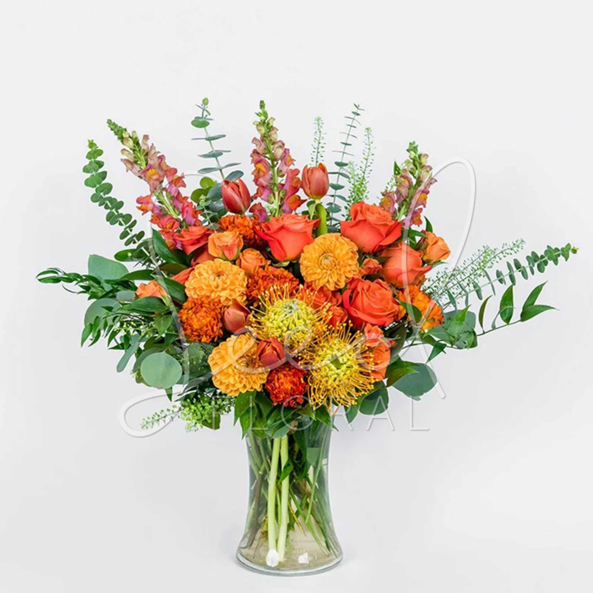 Tall arrangement of orange roses, marigolds, tulips and protea in a clear glass vase